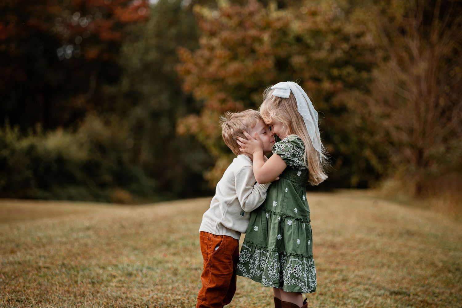 A couple in casual fall attire embraces in a golden autumn field during sunset.