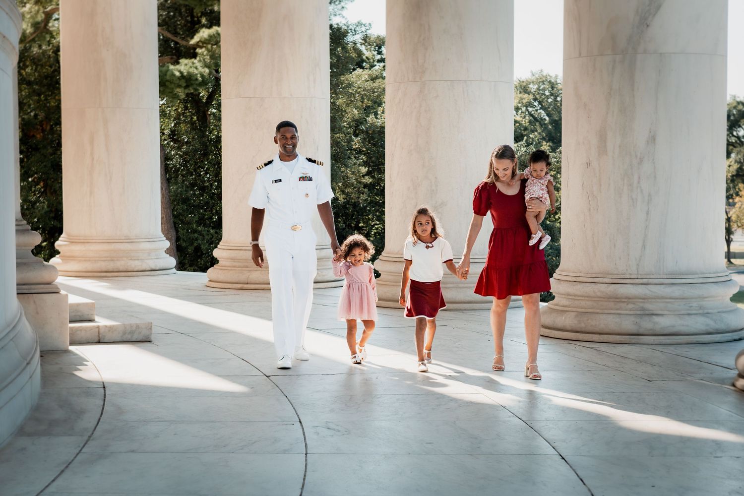 Family walking through sunlit columns at the Jefferson Memorial in Washington DC during a summer day.
