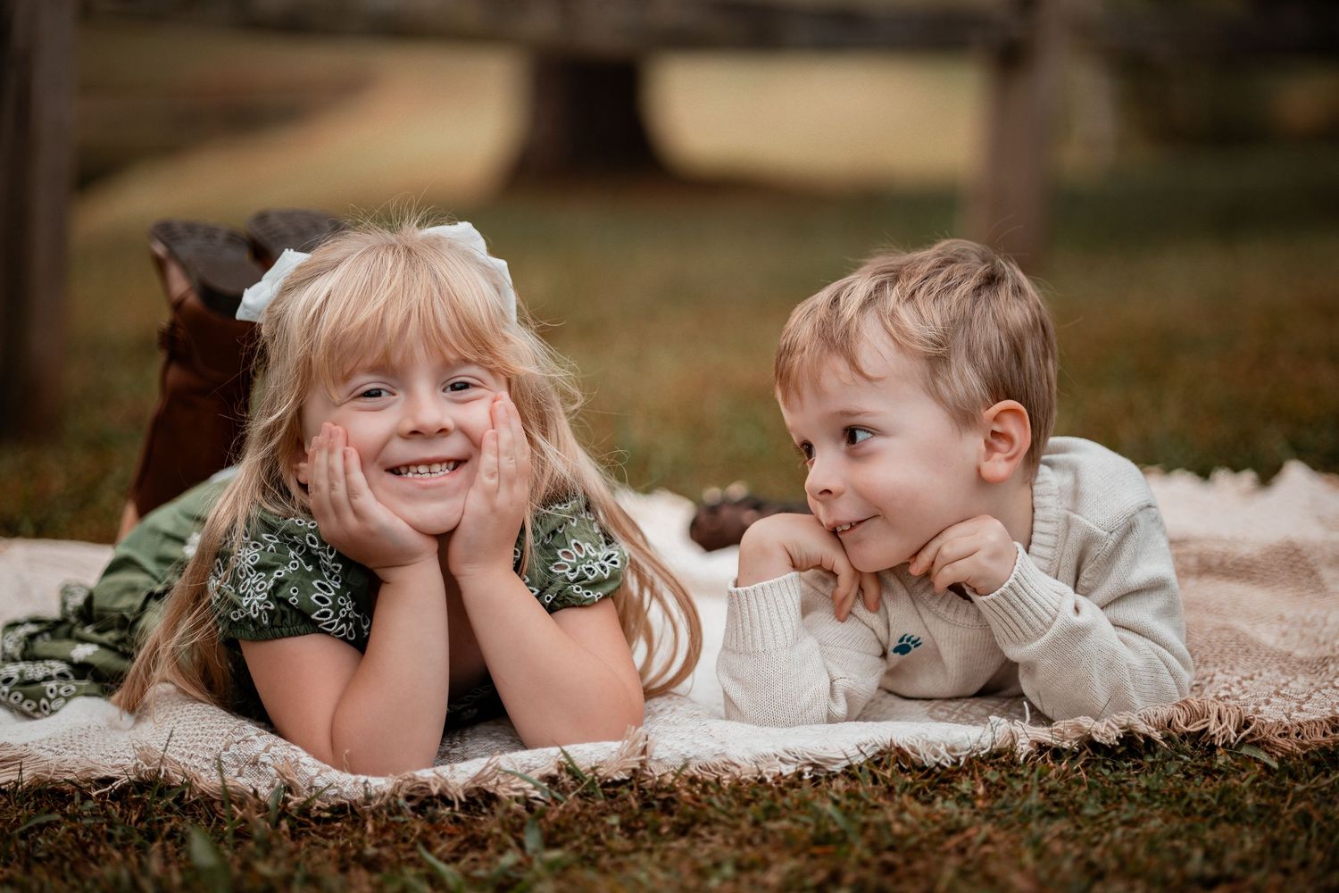 Two children lying on a blanket outdoors smiling and looking at each other during a photo session.