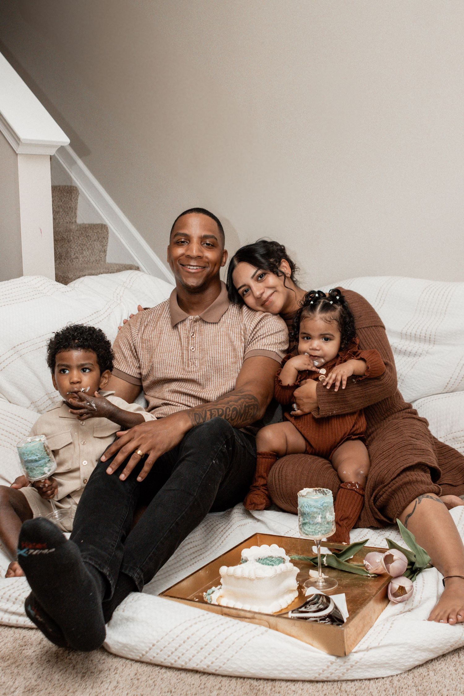 Family relaxes together on floor cushions with coffee and snacks in cozy home setting.