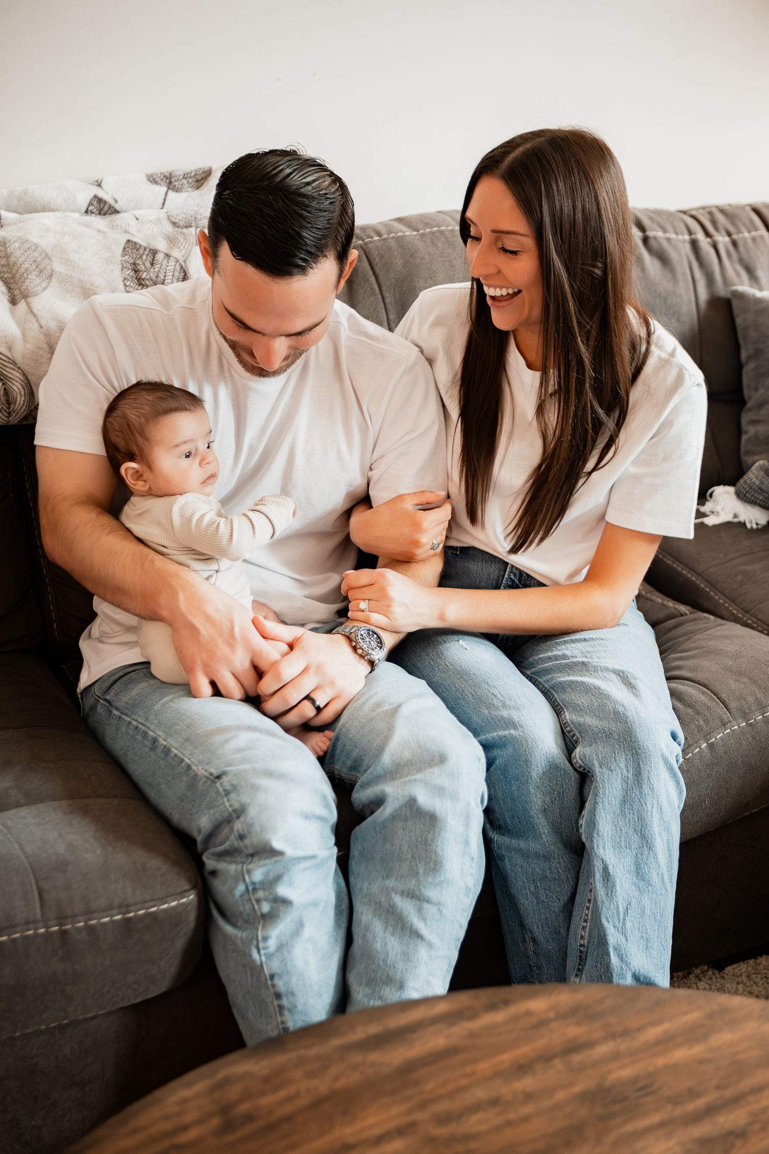 A family shares a sweet moment together on a grey couch in their living room.