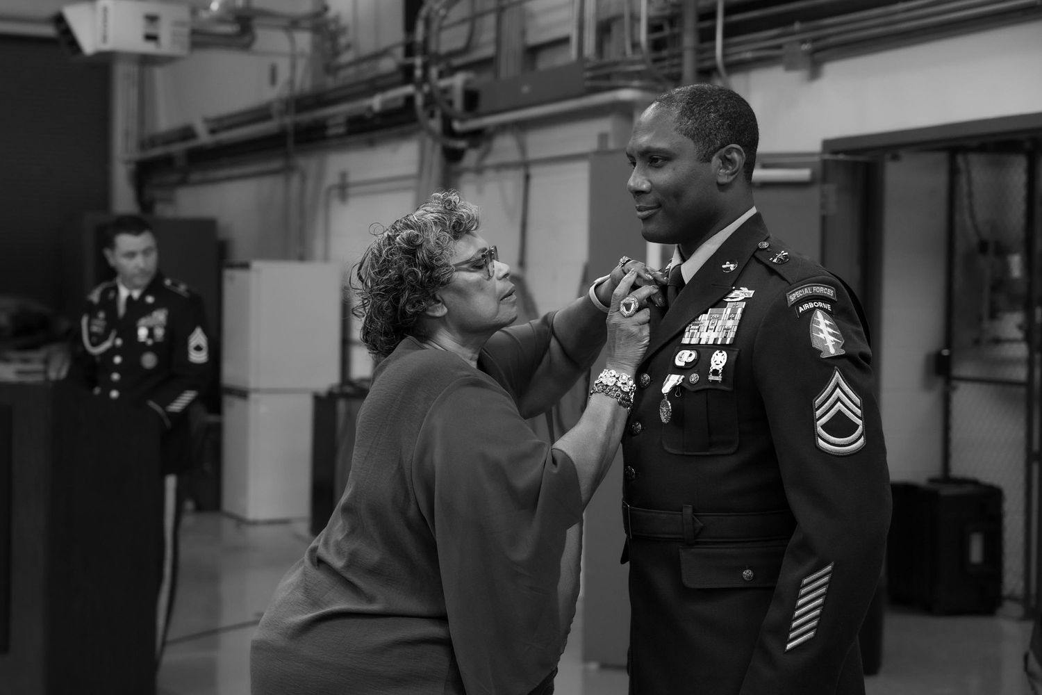 Woman pinning medal on decorated military soldier in dress uniform, black and white photo.
