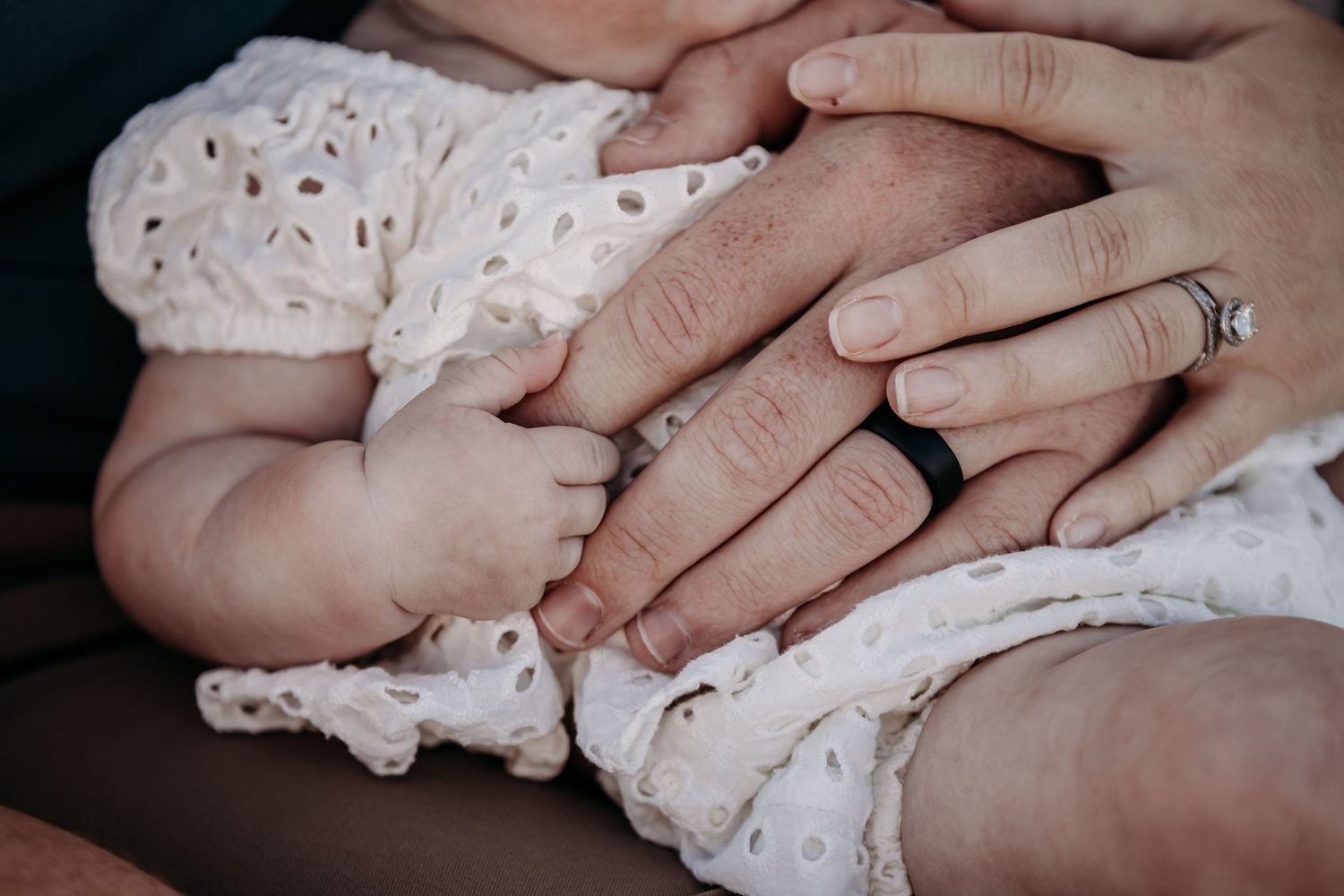 Close up of small baby hands holding adult fingers wearing an engagement ring.