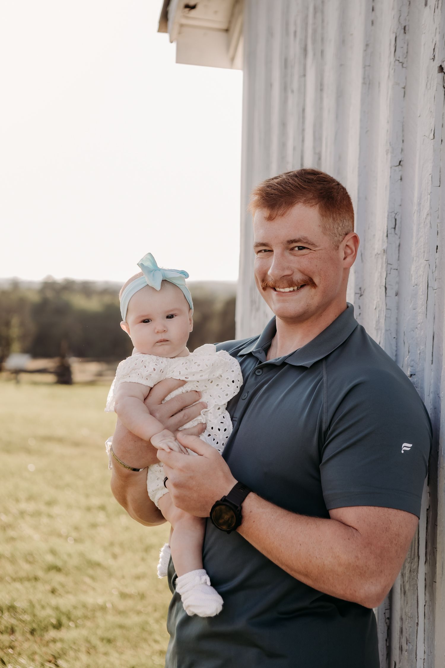A tender moment between an adult and baby against a white barn wall in natural lighting.