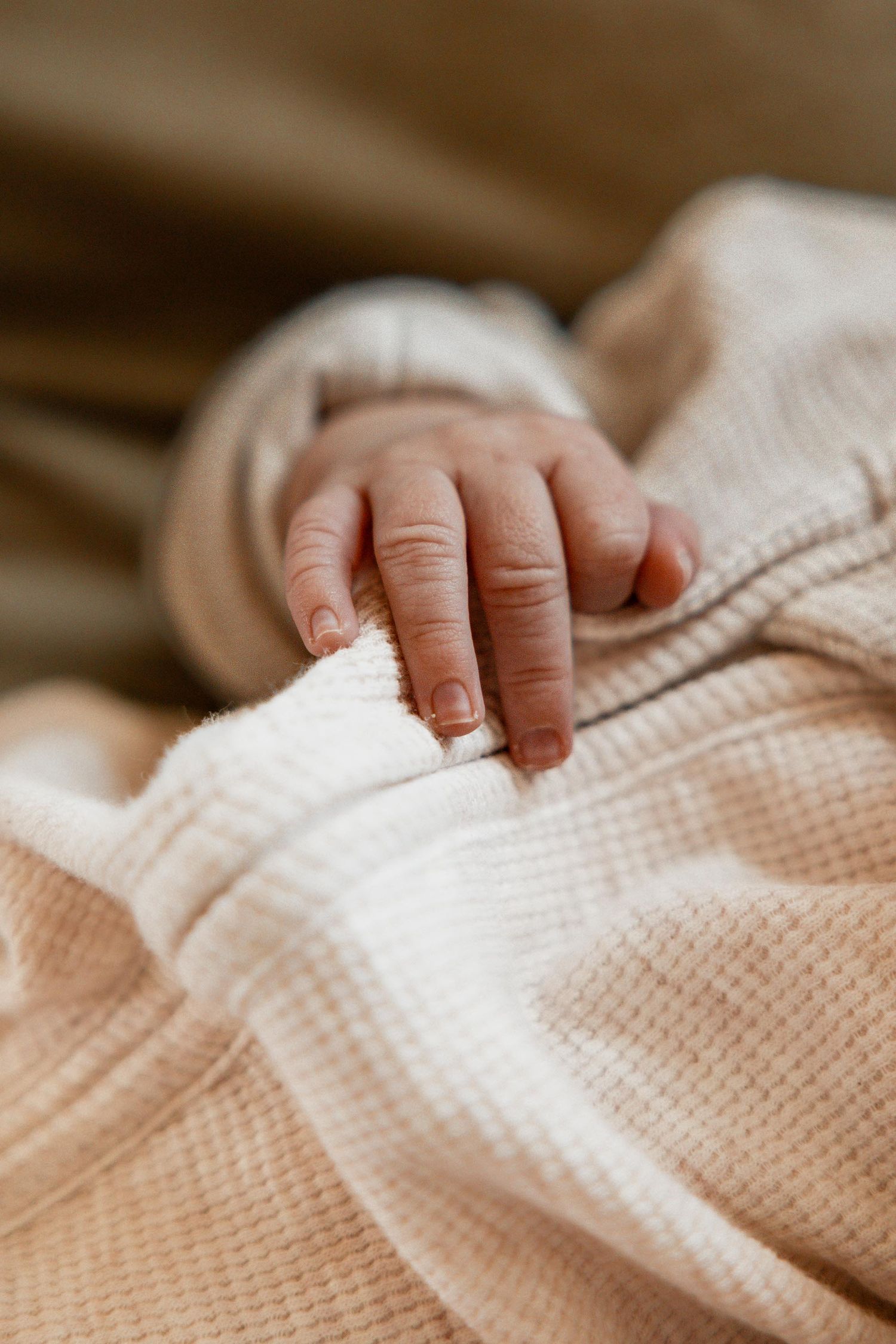 Close-up of a newborn baby's tiny hand resting on a soft waffle-knit blanket.