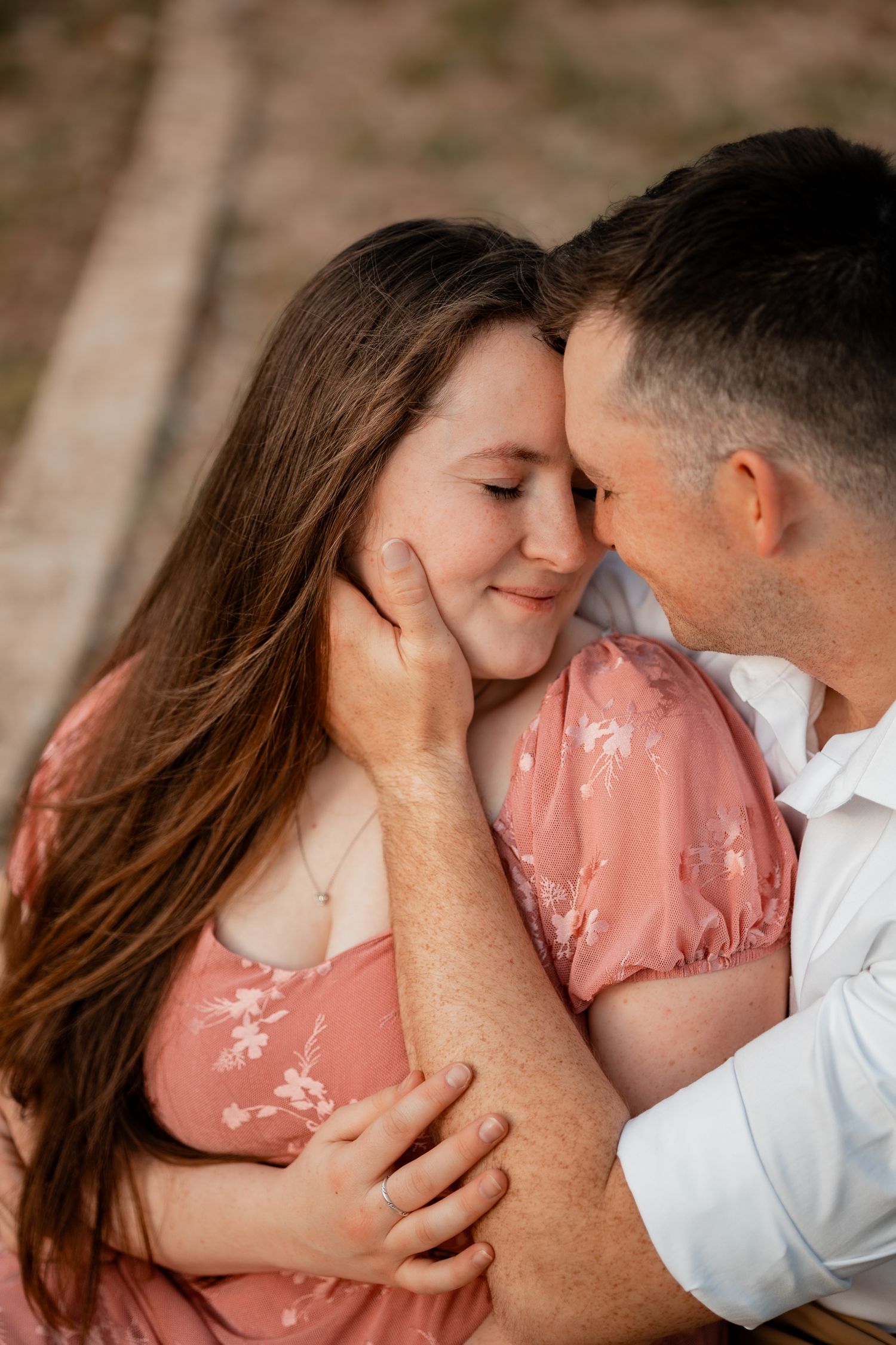 Couple sharing a tender moment, man gently cupping womans face as they touch foreheads outdoors.