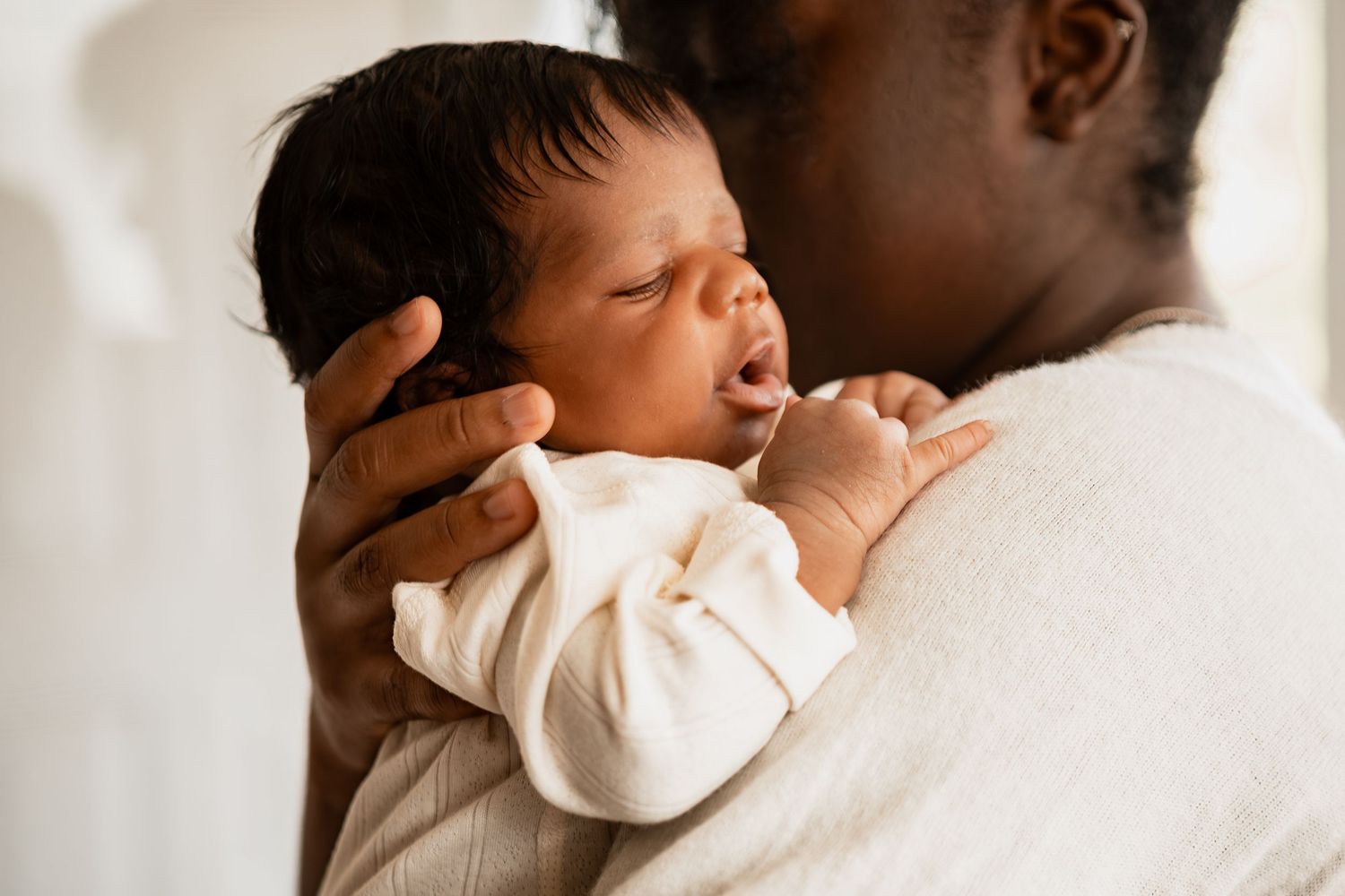 Tender moment between parent and newborn baby wrapped in white swaddle shown in black and white photography.