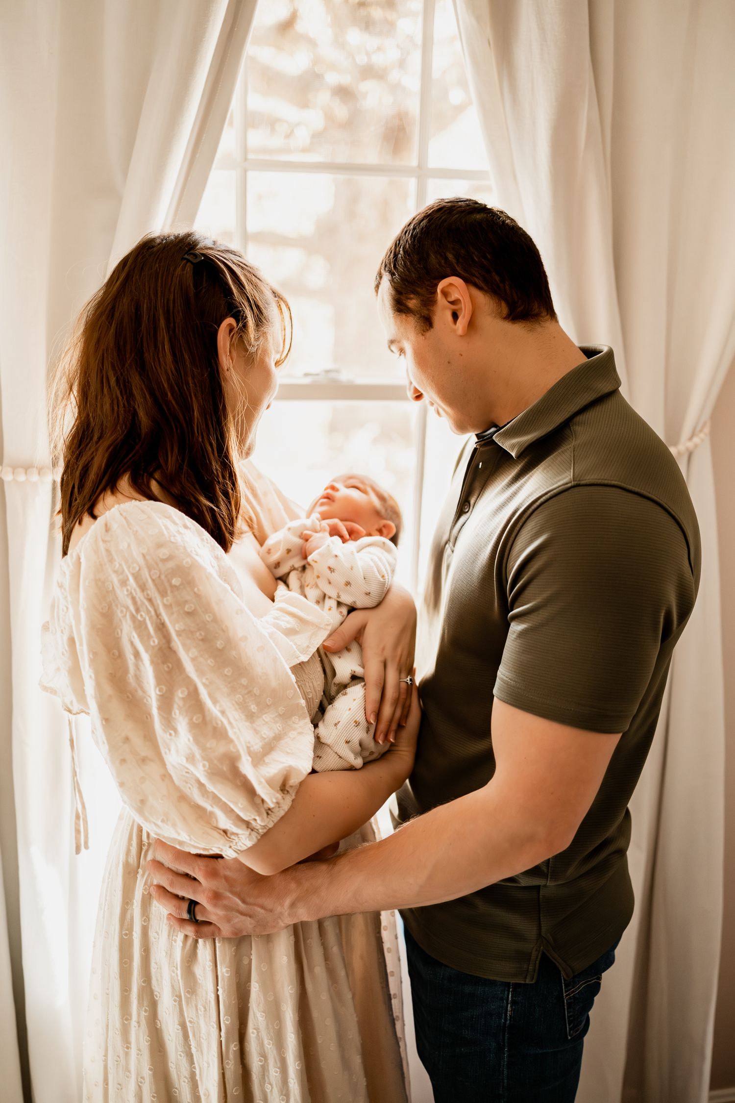 Three connected images show intimate moments between parents and their newborn baby against a bright window backdrop.