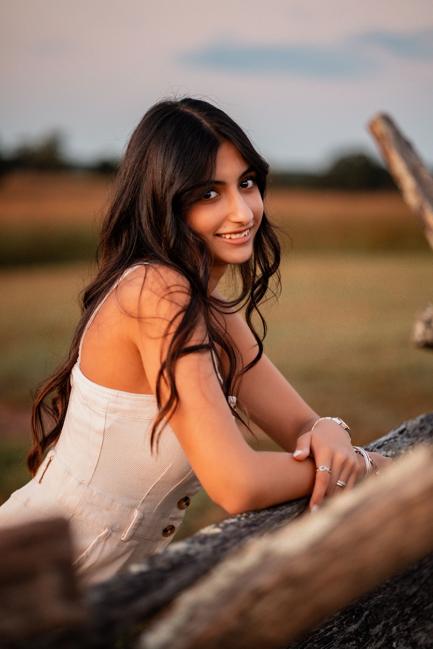 Summer portrait with white dress resting on rustic wooden log in warm sunlight.