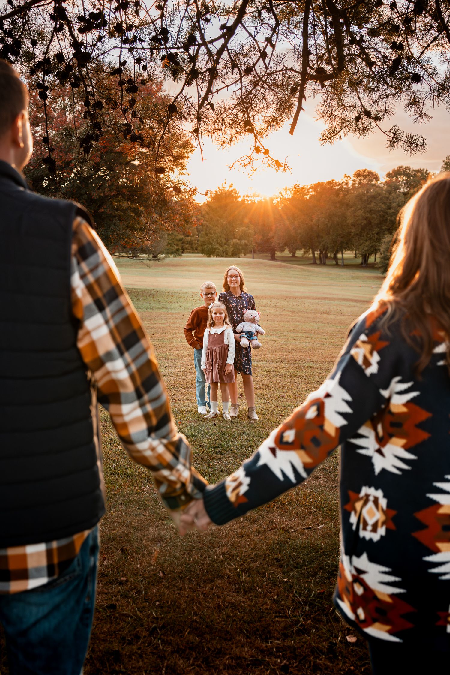 A couple holding hands walks in a field at sunset while wearing cozy plaid and patterned blankets.