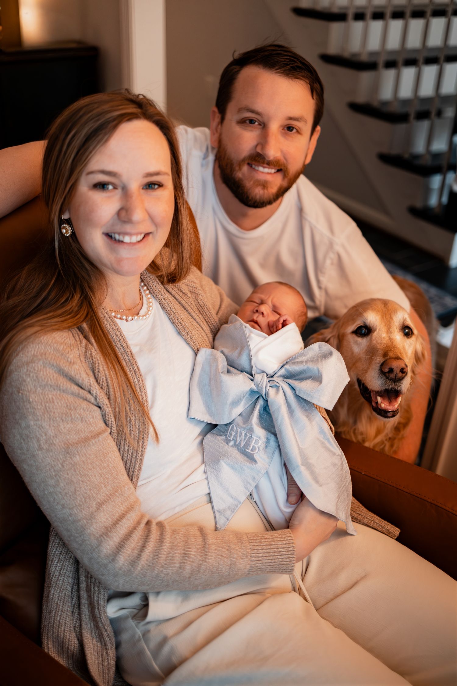 Family portrait with newborn baby and golden retriever dog sitting on stairs.