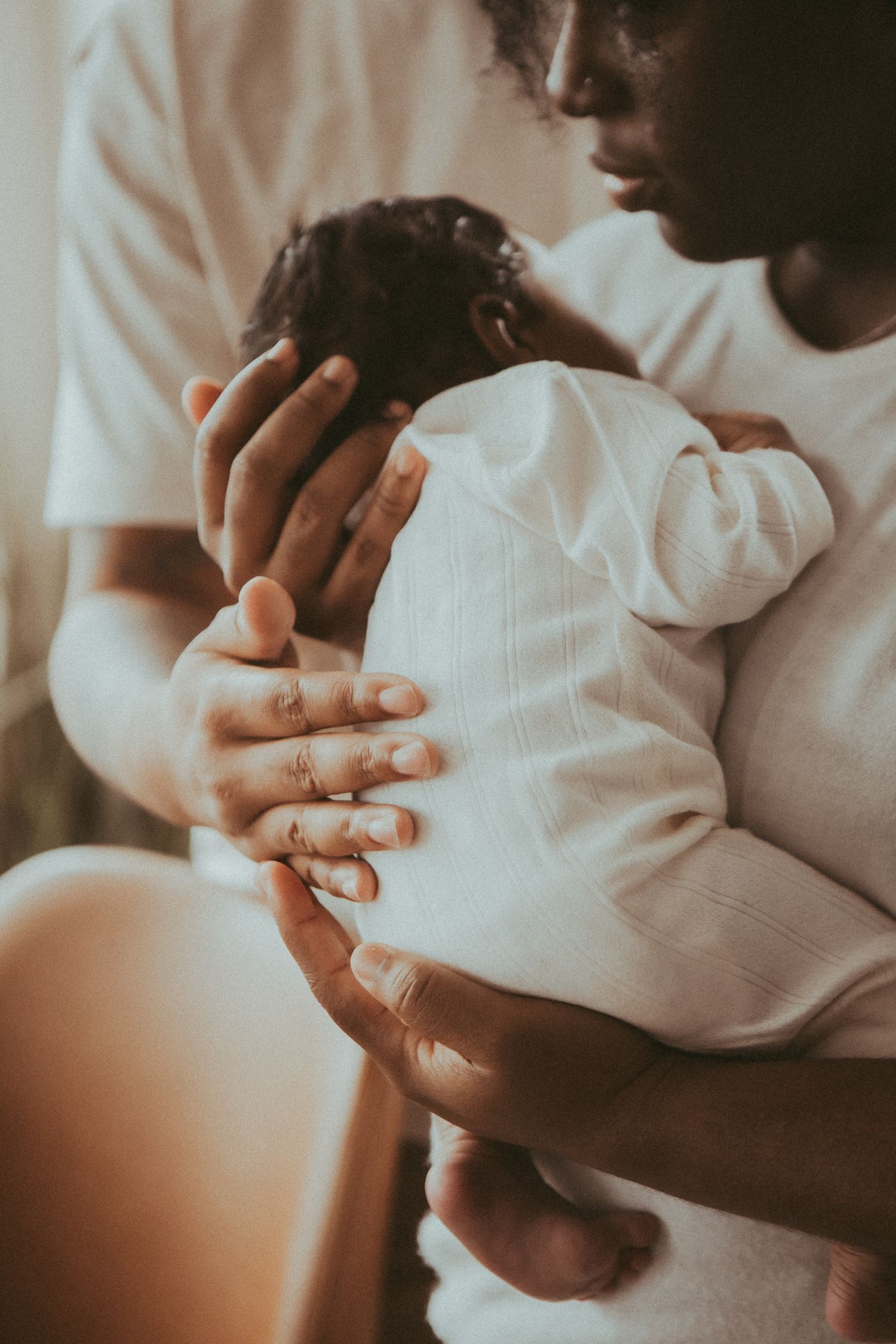 Tender close-up shot of parent holding newborn baby's tiny hand in warm lighting.