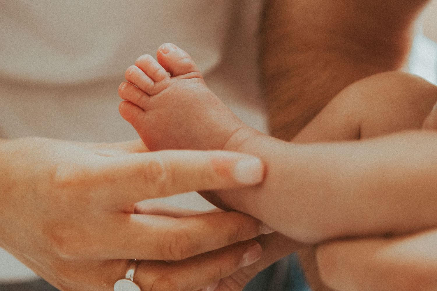 Gentle hands tenderly hold a tiny baby foot in a warm, intimate moment.