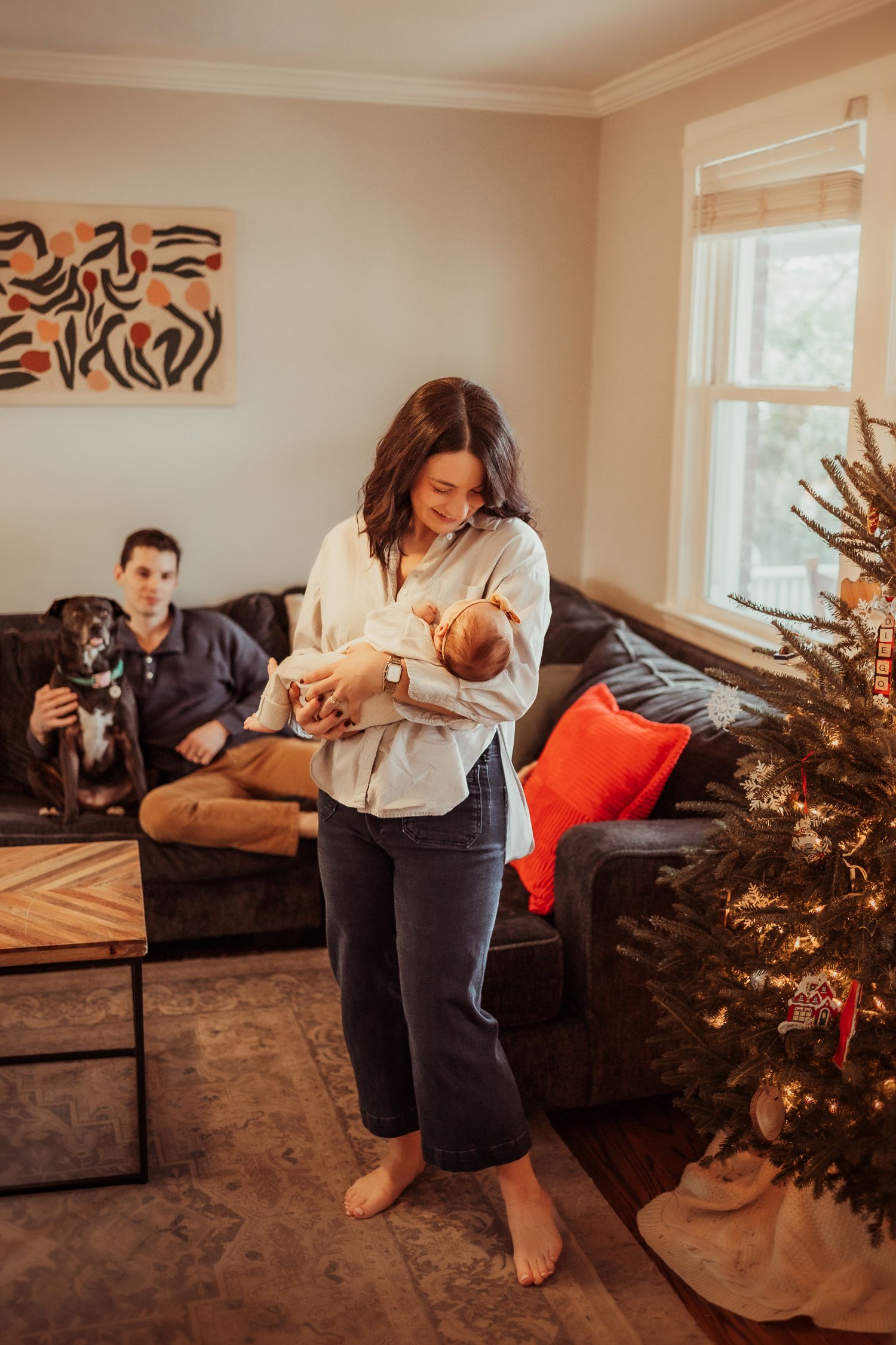 A cozy living room scene with a decorated Christmas tree, while people and a dog relax on the brown couch.