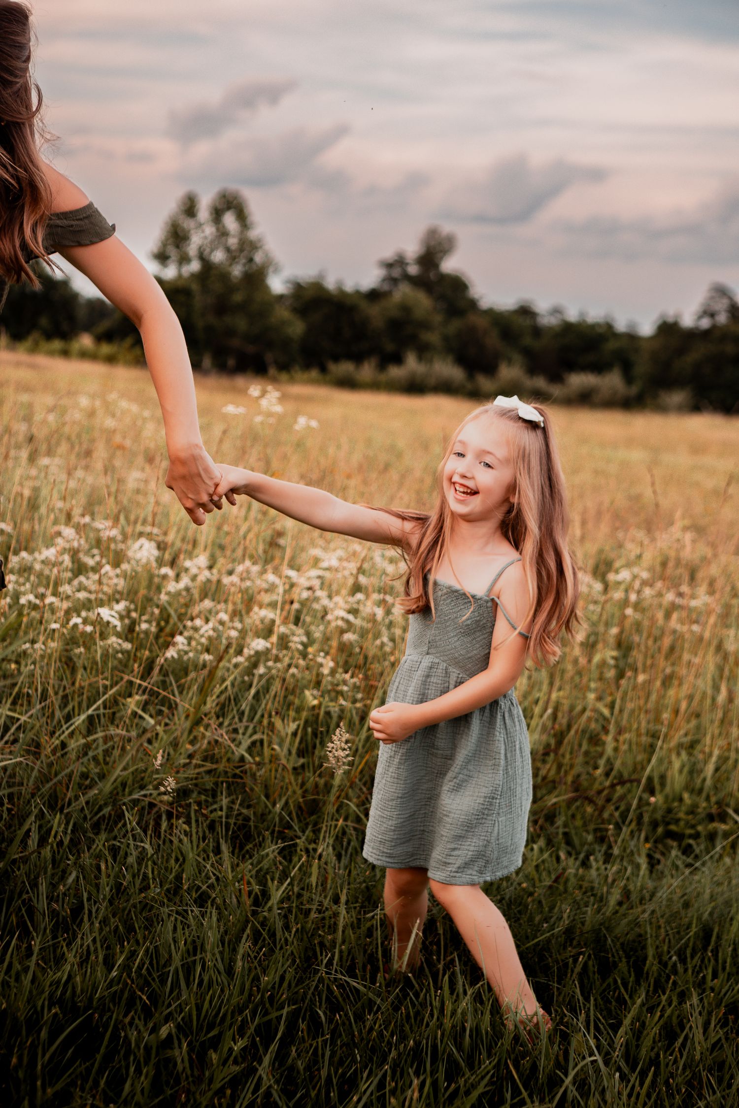 A series of joyful poses in a meadow at sunset shows a child in a gray dress spinning and dancing among wildflowers.