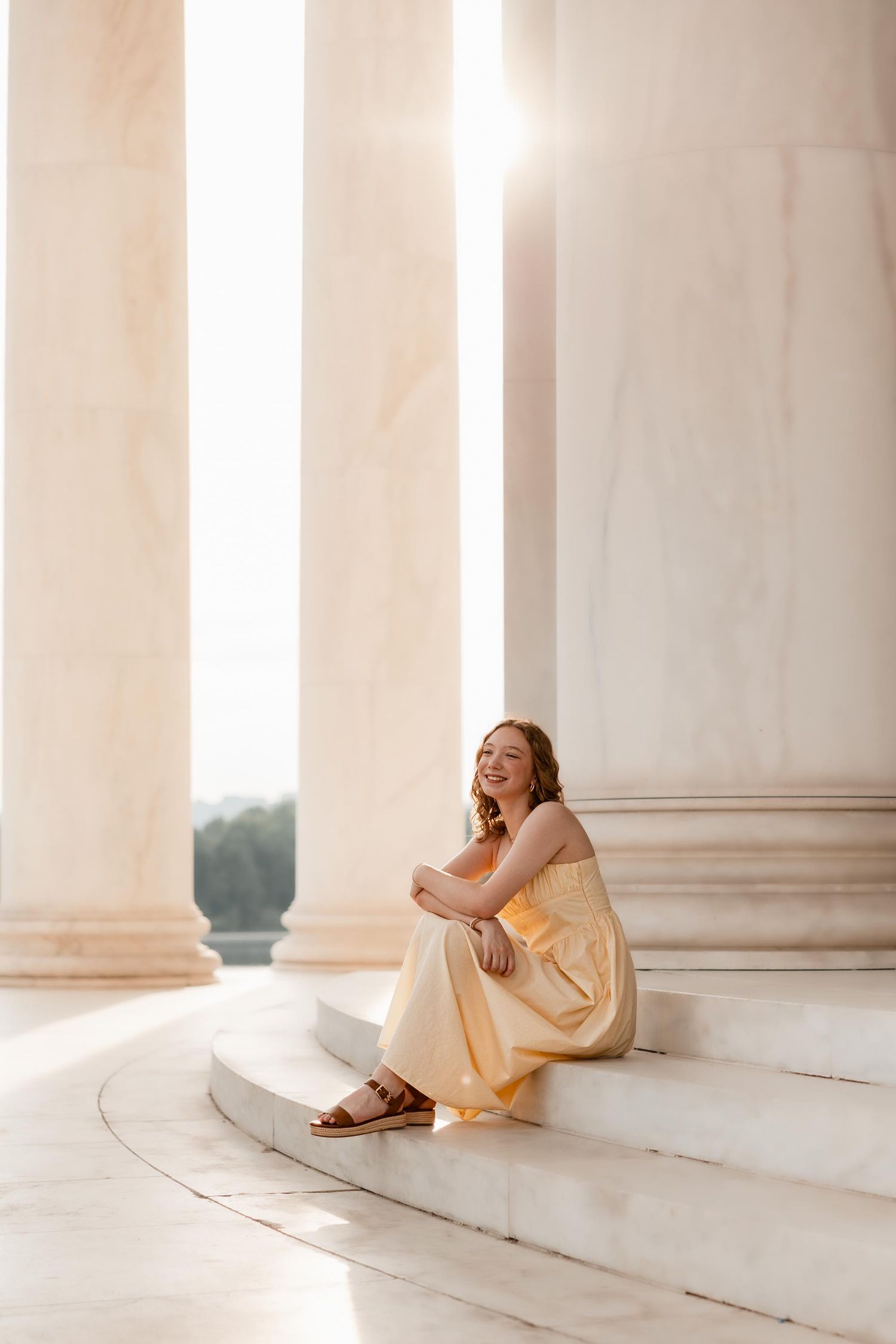 Young woman in yellow dress sitting on marble steps between tall columns at the Jefferson Memorial.