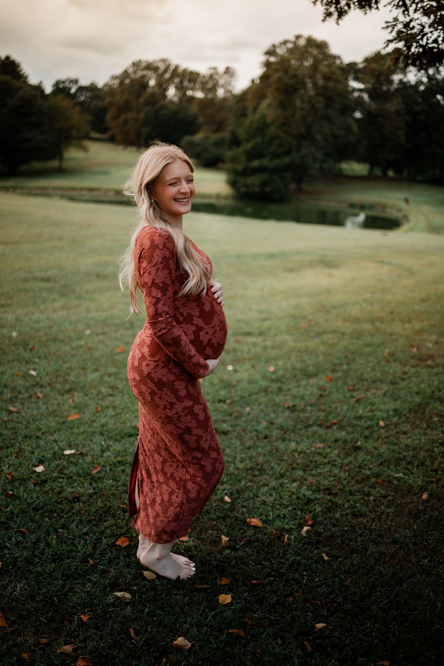 A person in a rust-colored dress twirls playfully in a grassy field at sunset.