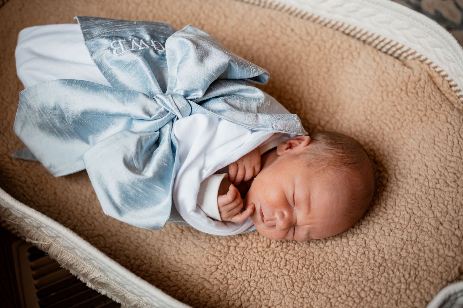 A newborn baby sleeps peacefully wrapped in a soft blue blanket on a beige textured surface.
