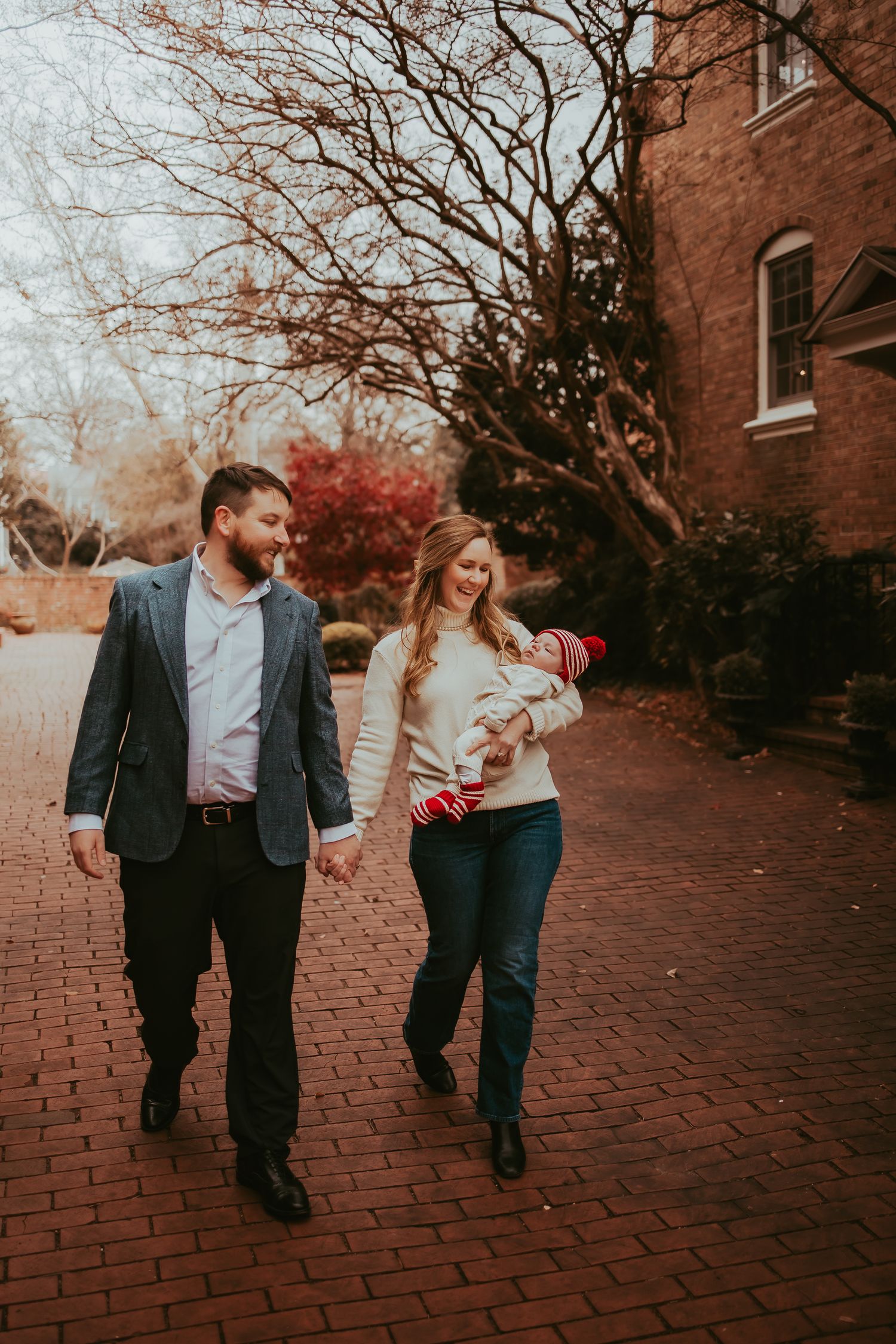 A couple walks and laughs together on a red brick path surrounded by autumn trees and brick buildings.