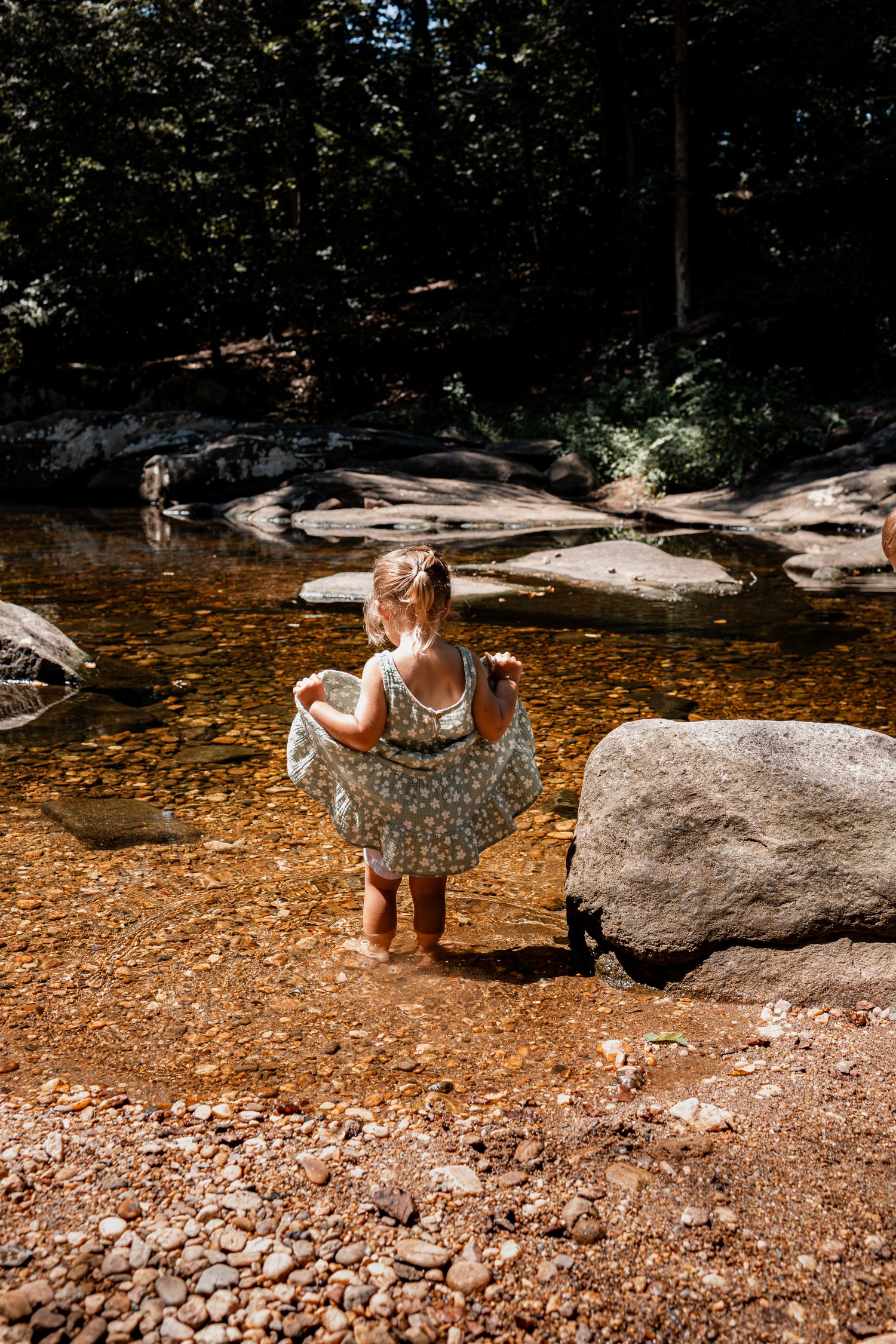 Woman in a polka dot sundress enjoys a summer day by a natural stream with smooth rocks and golden-tinted water.