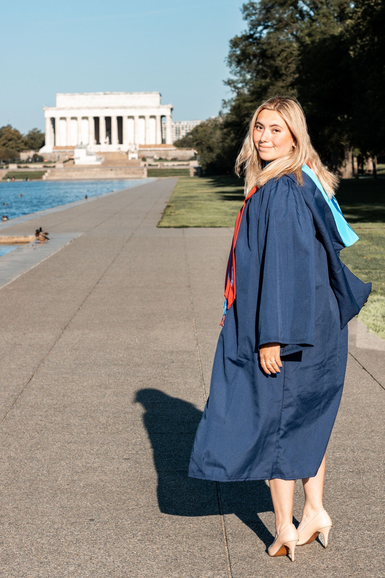 Graduate in blue gown walks along the reflecting pool with the Lincoln Memorial visible in the background.