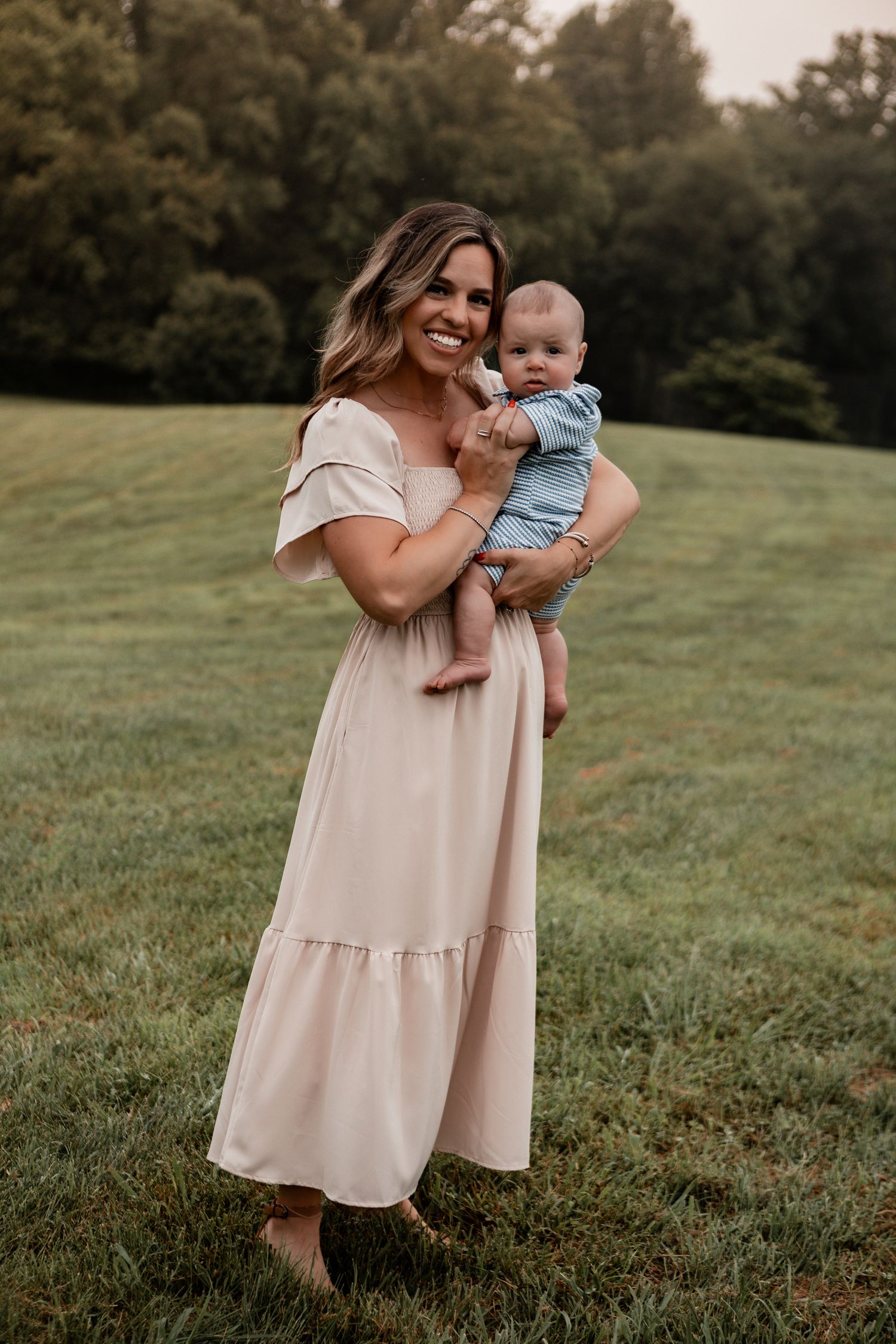 A gentle interaction in a cream-colored dress against a lush green field at dusk.
