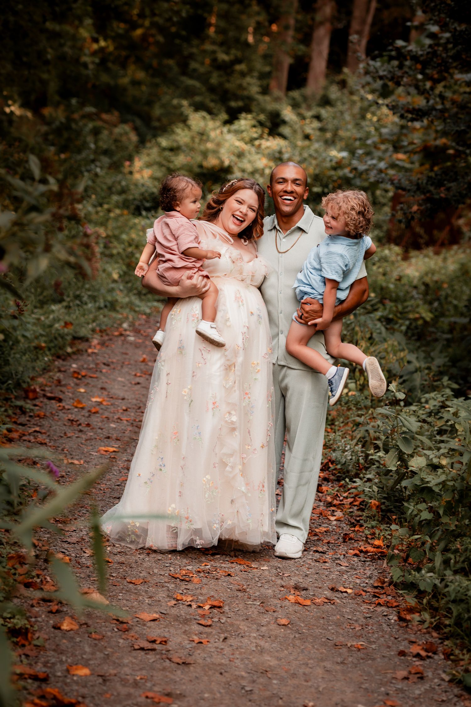 A family shares joyful moments together on a wooded path covered in autumn leaves during a photo session.