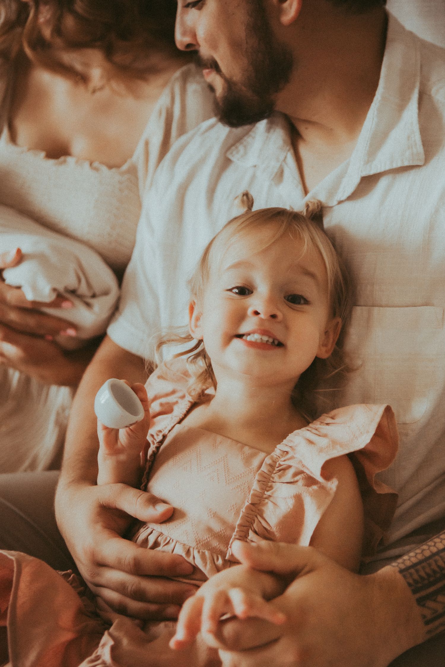 A series of warm-toned photos showing tender moments between parent and child lying on white bedding.