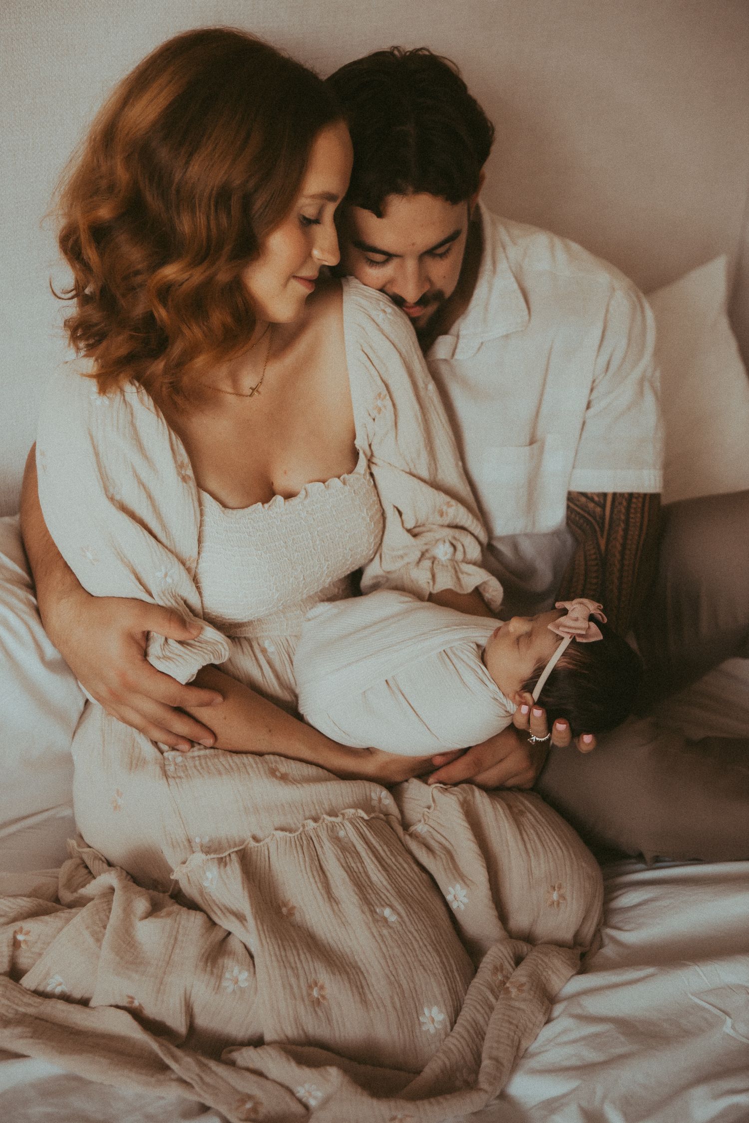 Intimate family moments captured in soft muted tones as they cuddle together on a bed in matching white outfits.