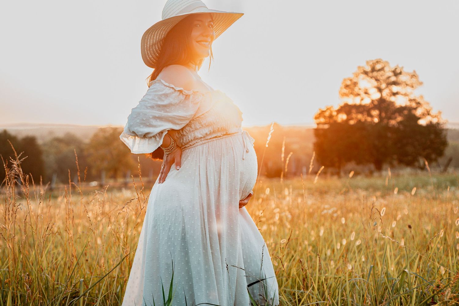 Sun illuminates a figure in a white dress and orange hat twirling in a golden wheat field at sunset.