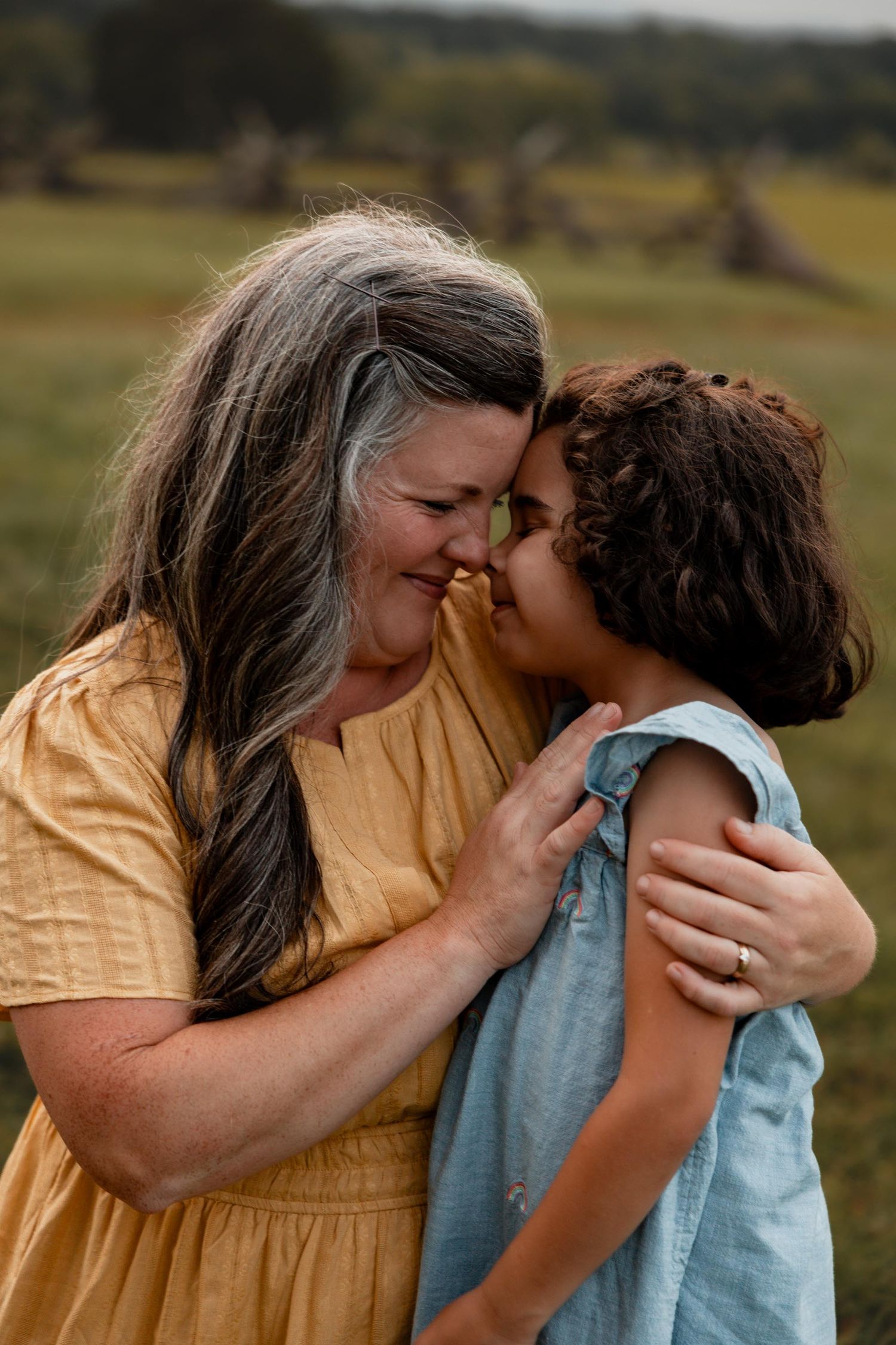 A loving mother and young daughter share a tender nose-to-nose moment in an open green field.