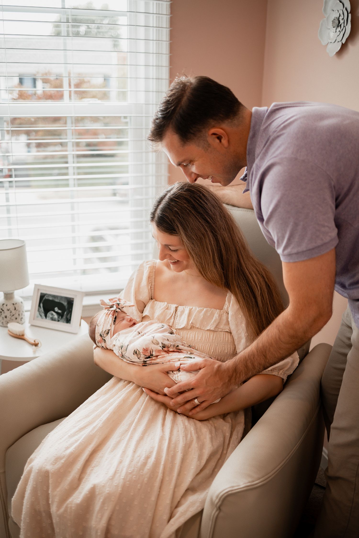 A tender moment captured on a beige couch as parents cradle their newborn baby in soft natural lighting.