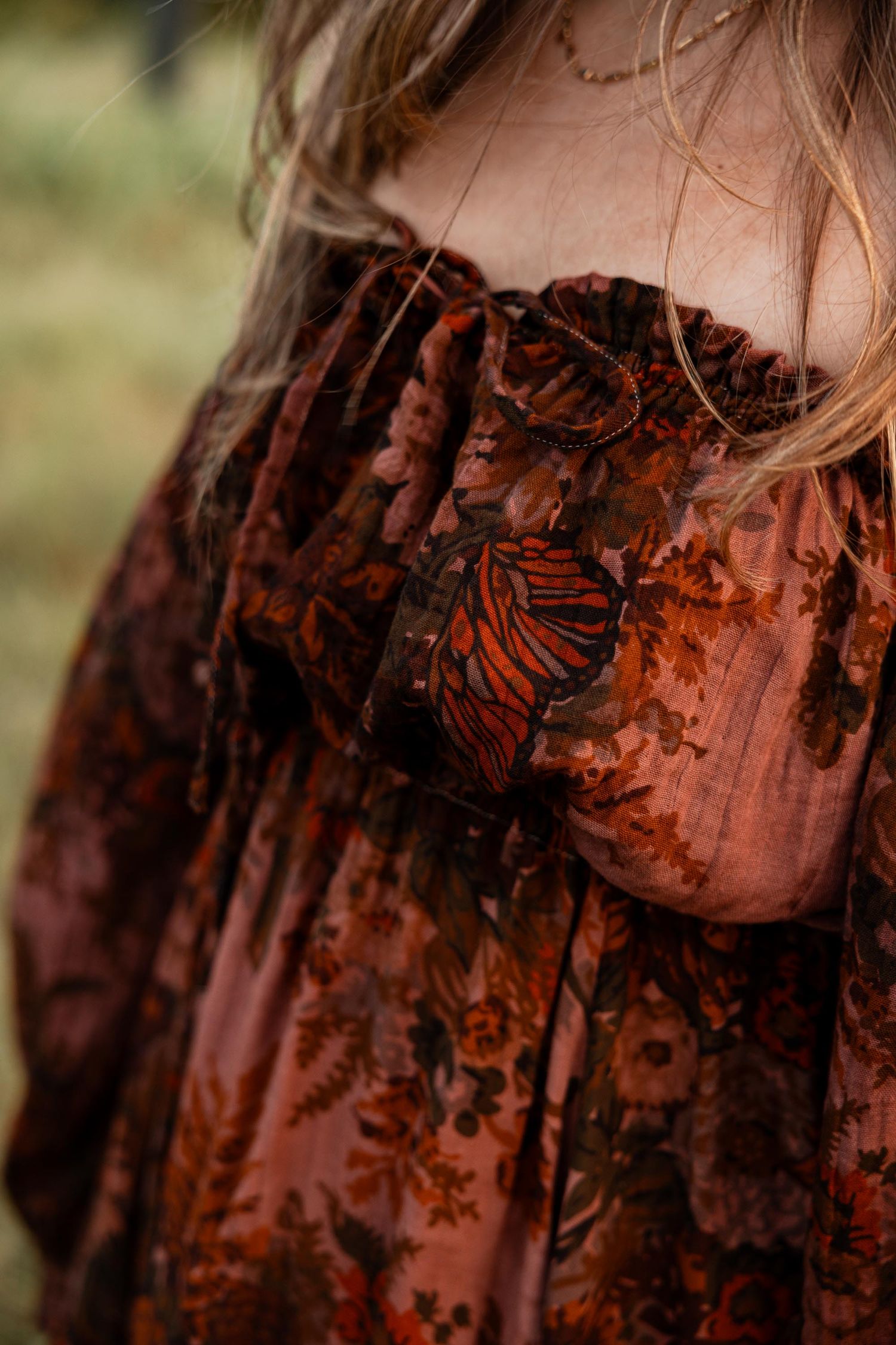 Close-up of a child wearing a rust floral velvet dress with ruffled neckline and butterfly detail.