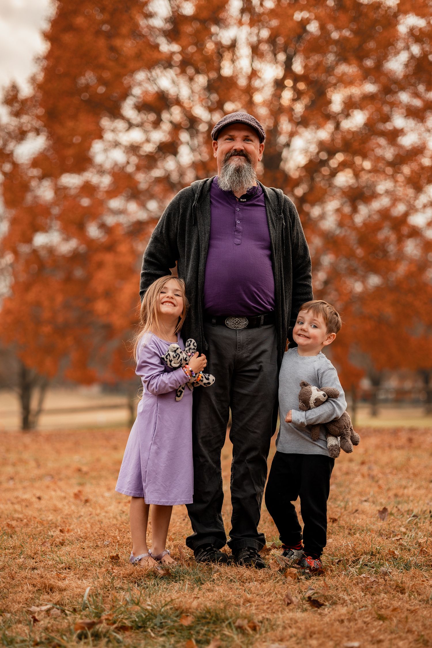 A heartwarming autumn family portrait with two children and an adult standing among orange-leaved trees.