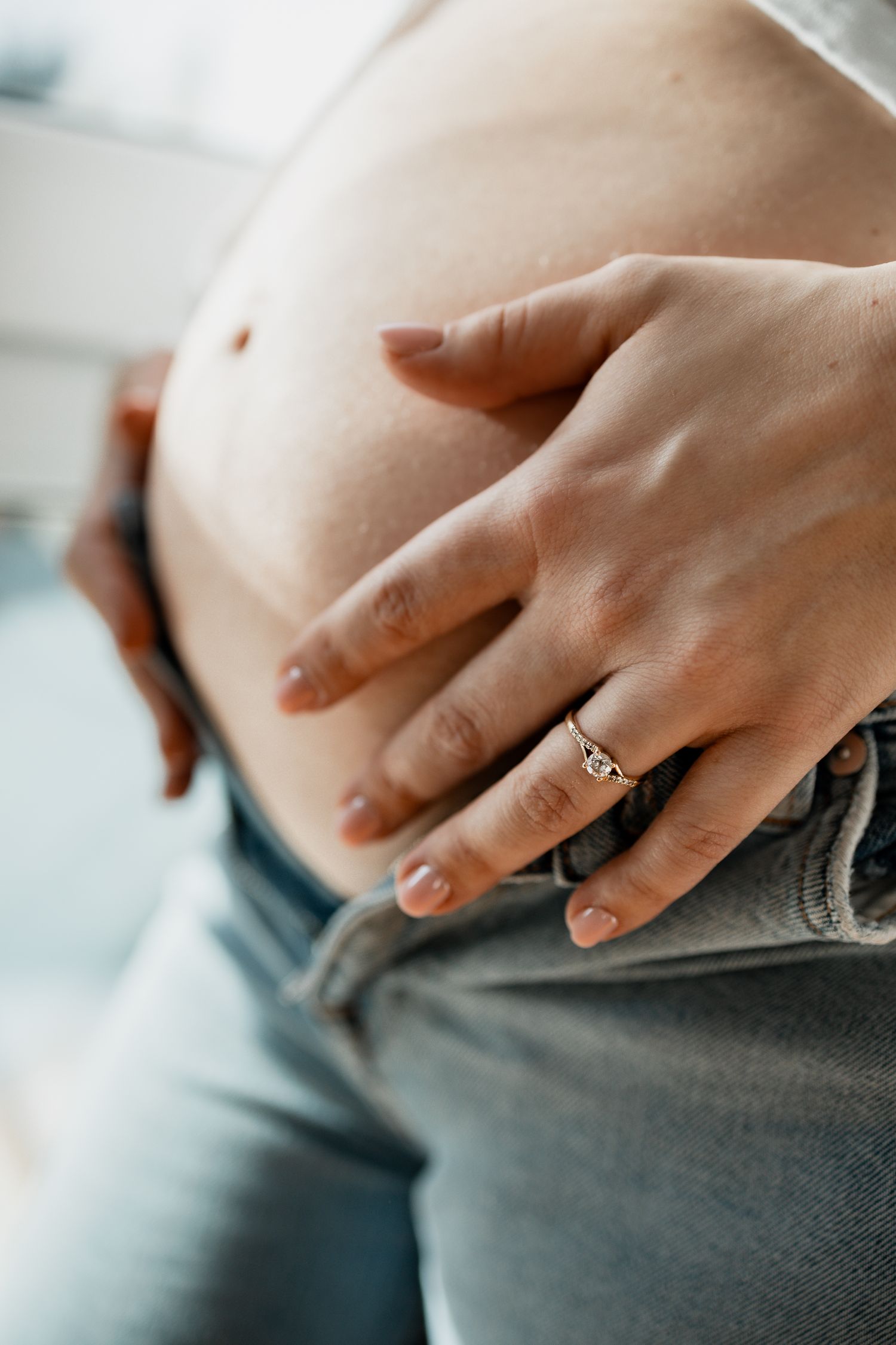 Close-up shot of hands wearing a delicate ring against a soft gray background.