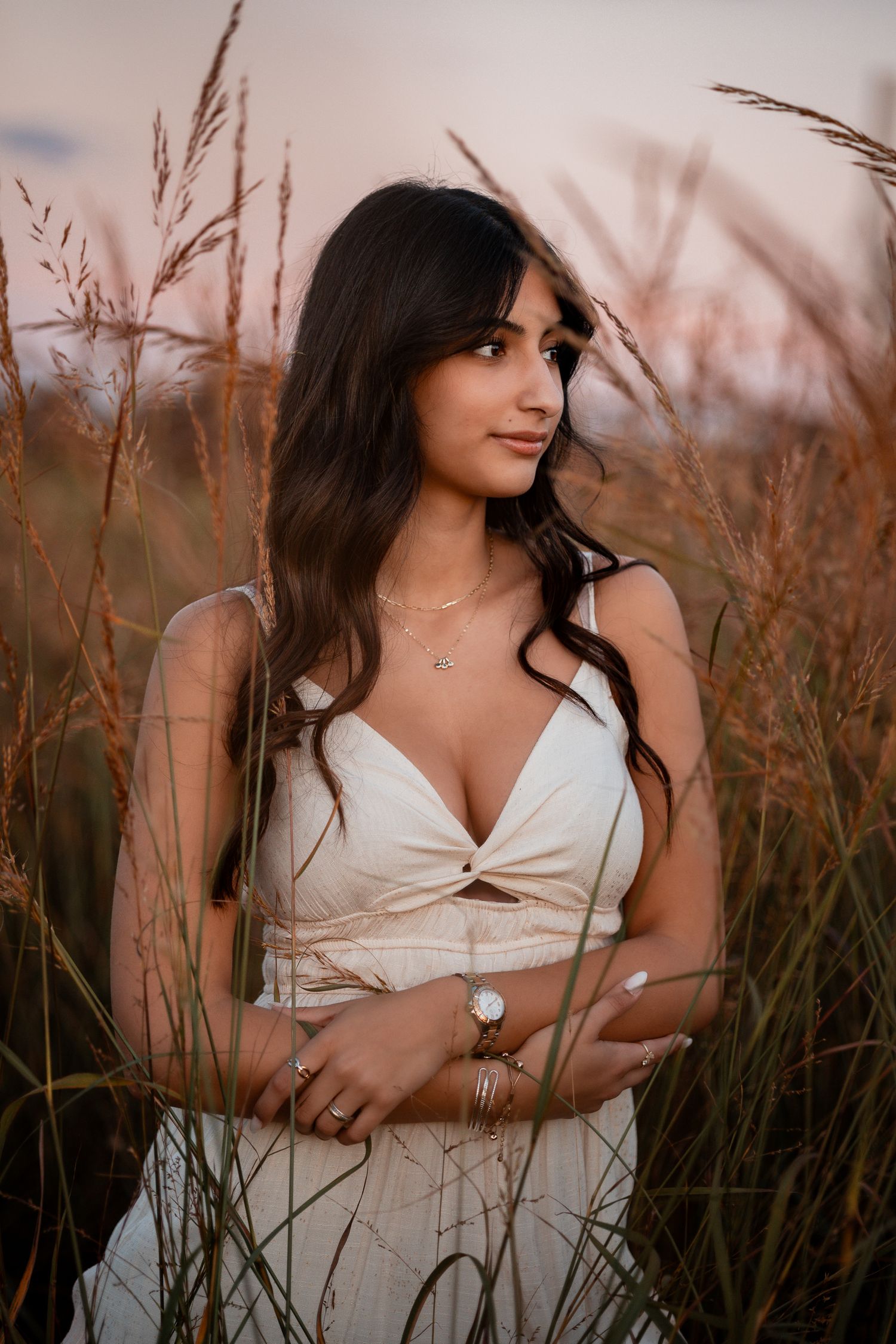 Portrait session in a field at sunset with subject wearing white dress among tall grass.