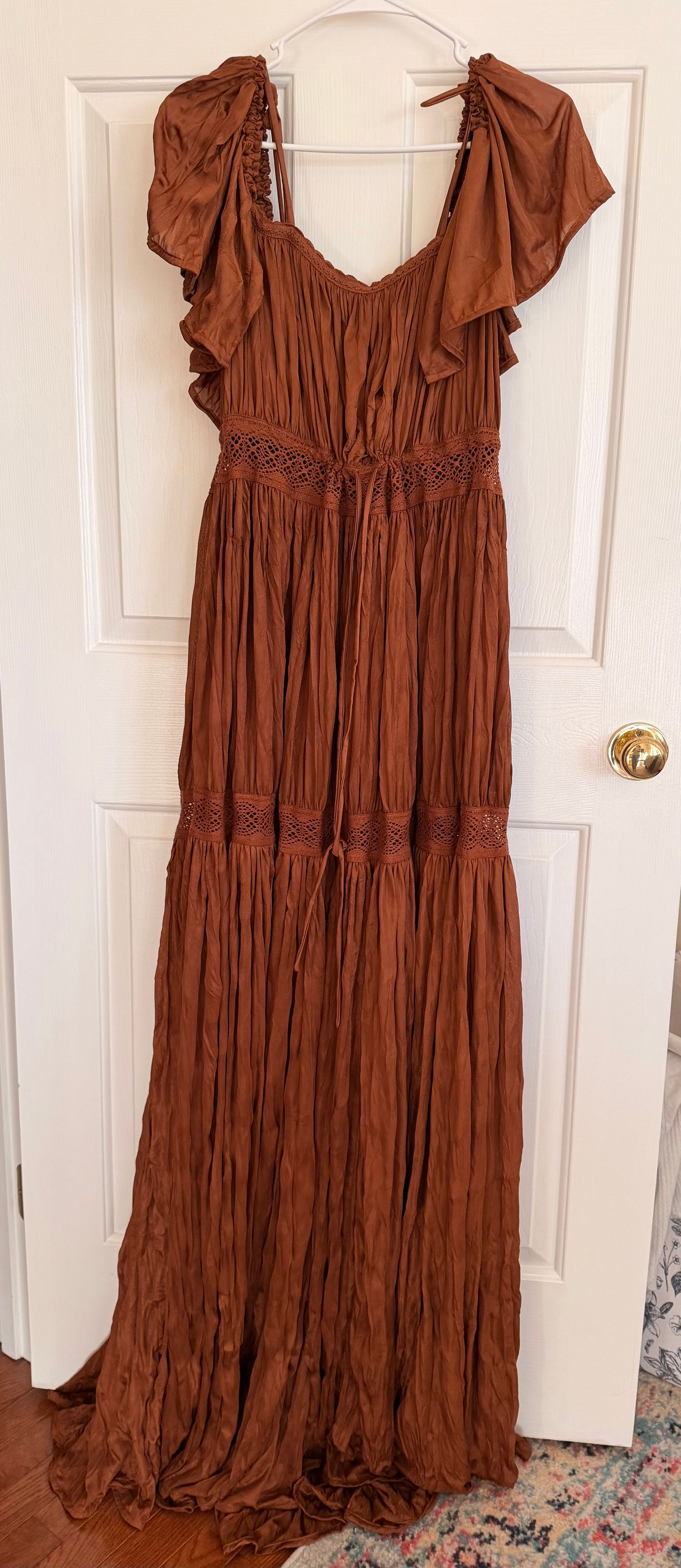 A rustic brown tiered maxi dress with ruffled details and cap sleeves displayed against a white door.