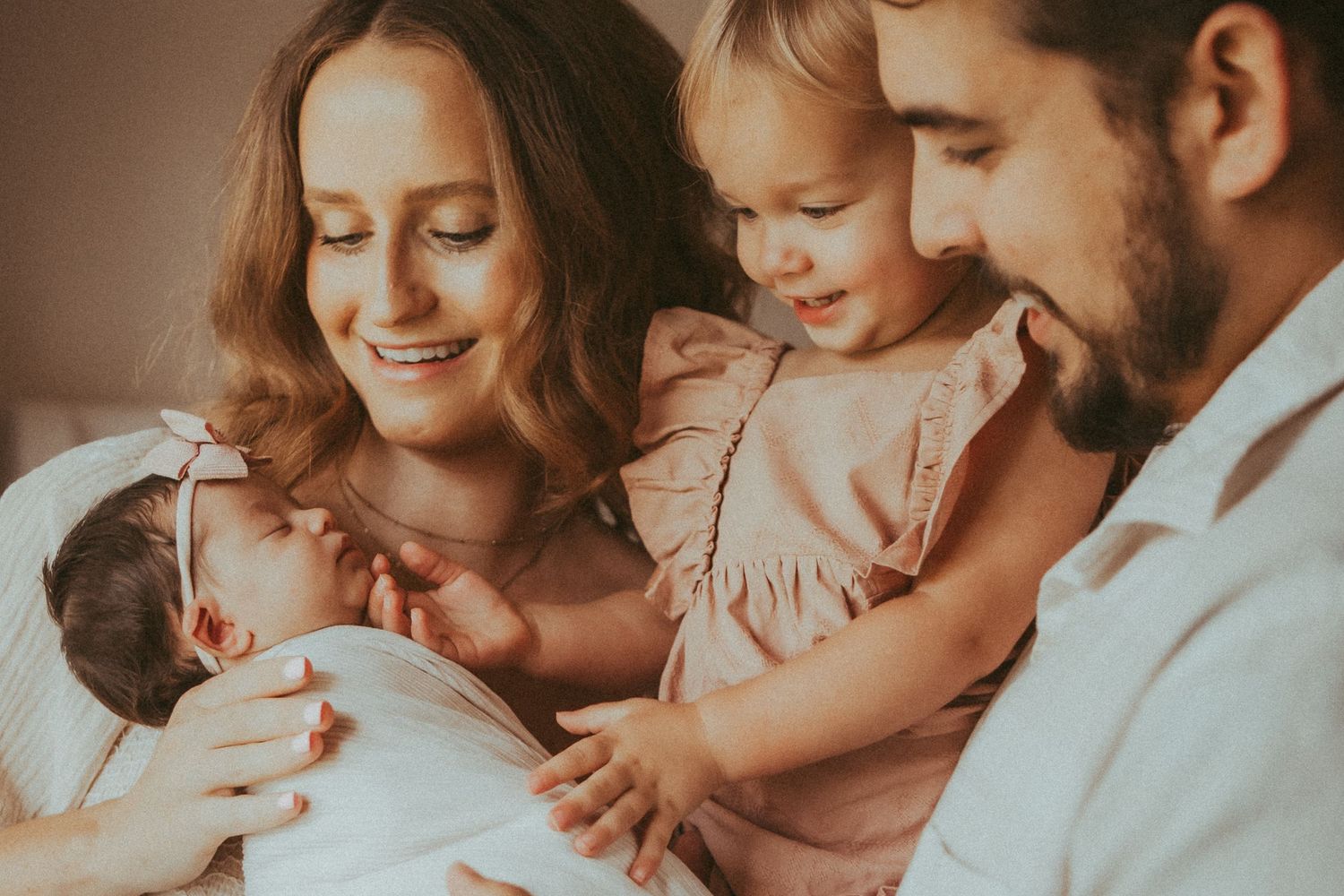 A family shares an intimate moment together on a bed in warm lighting.