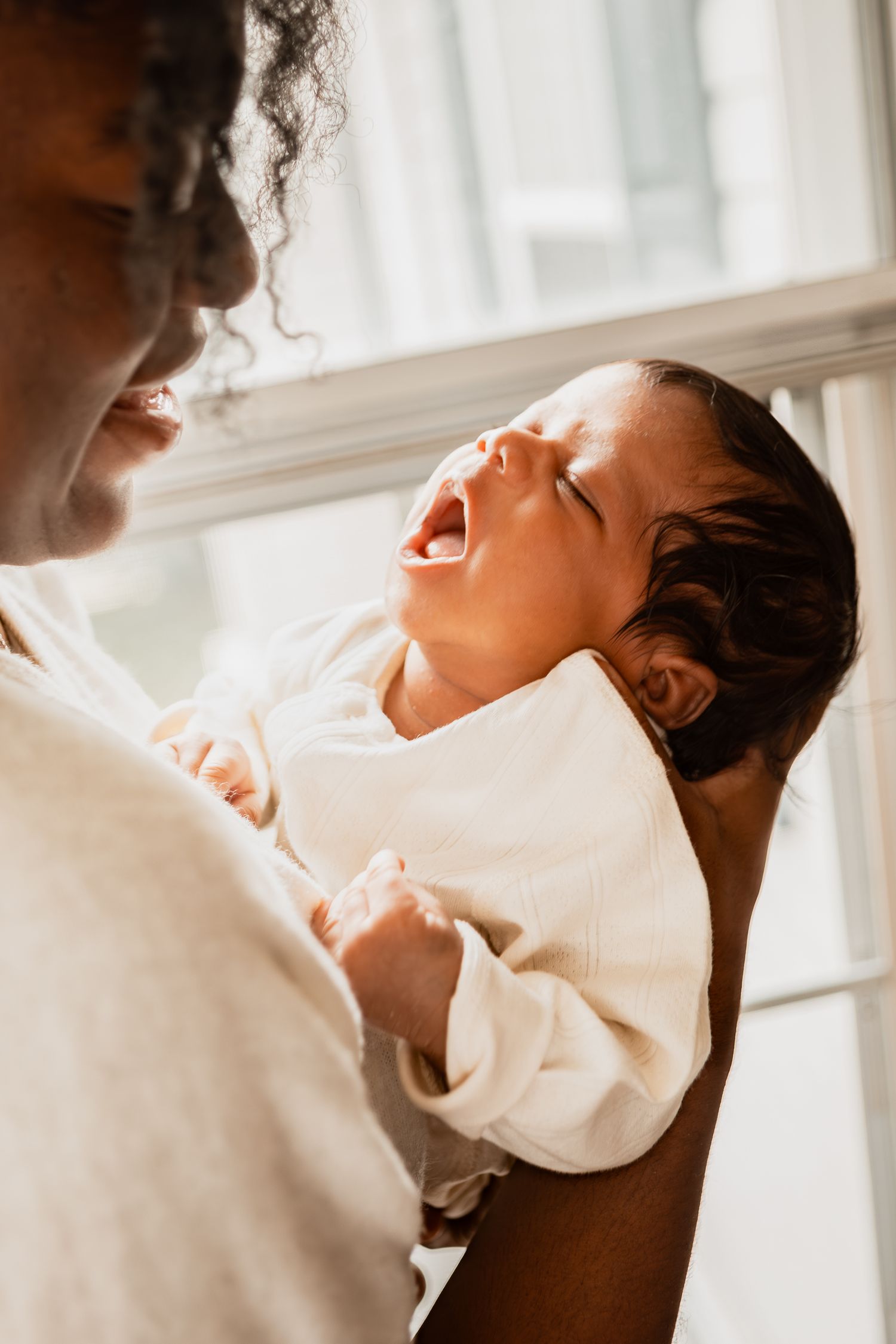 Parent holding sleeping newborn baby against white shirt in soft natural window light.