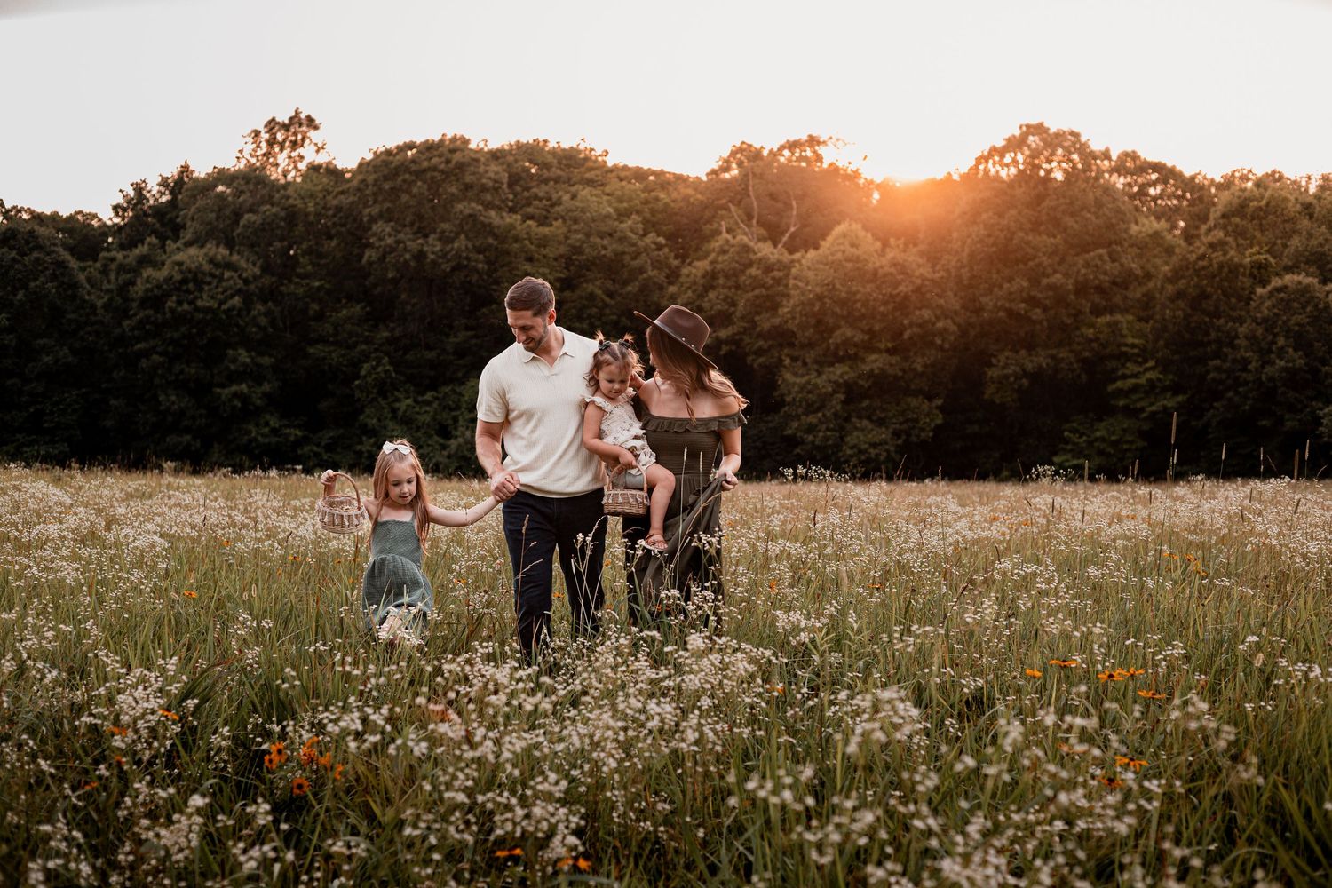 A family enjoys a warm sunset together in a wildflower meadow during golden hour.