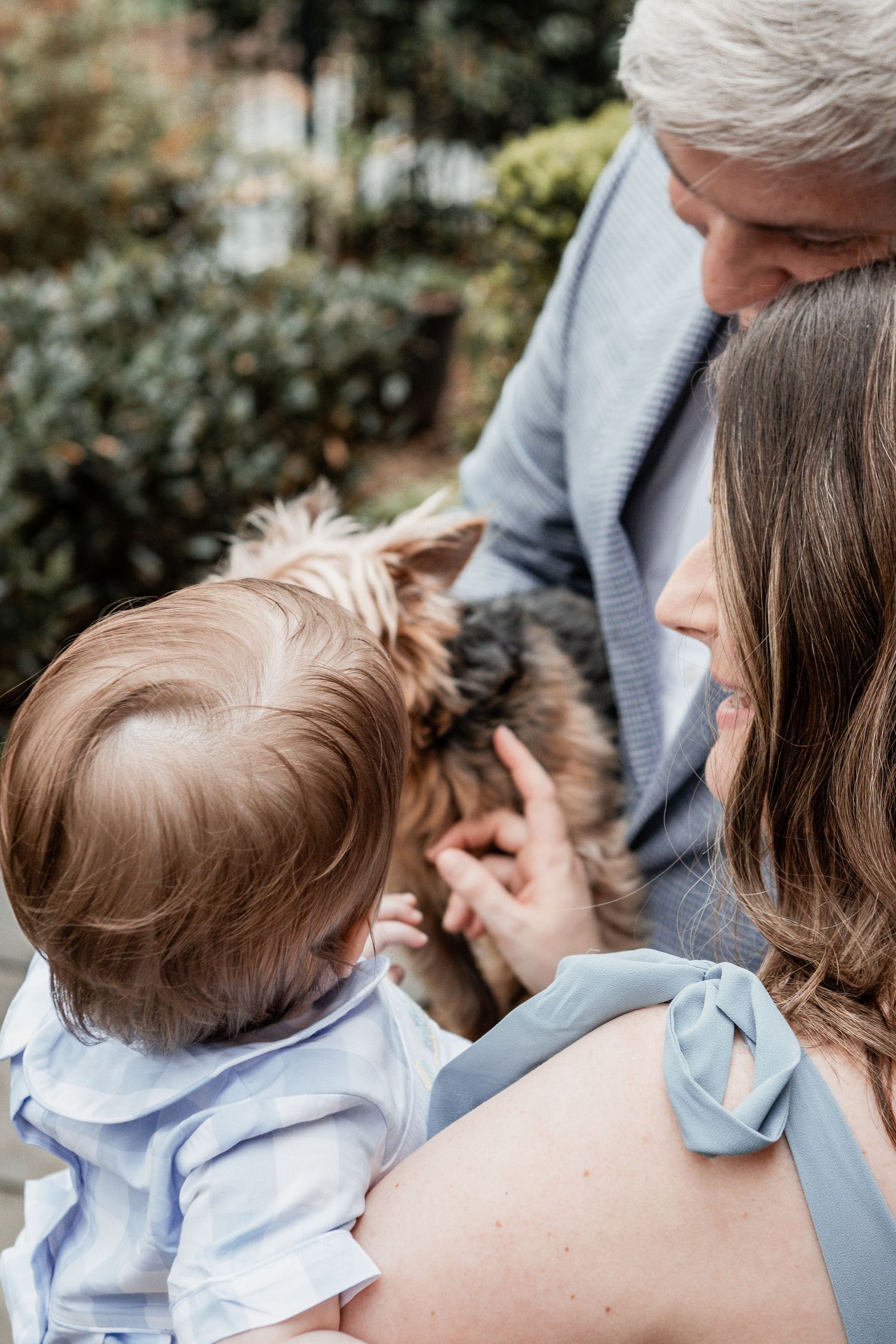 A family sharing a tender moment outdoors while holding a small child in a light blue shirt.