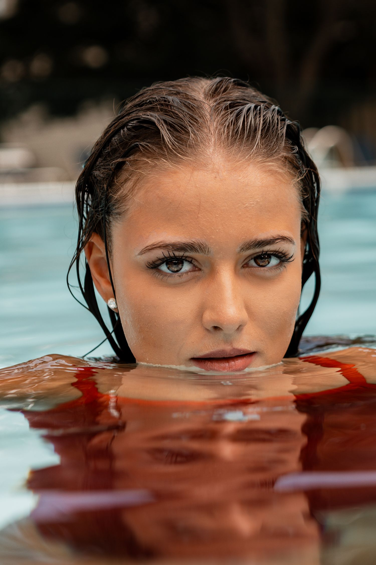 An artistic portrait photograph taken in water shows a cropped view of a face with intense blue eyes half-submerged.