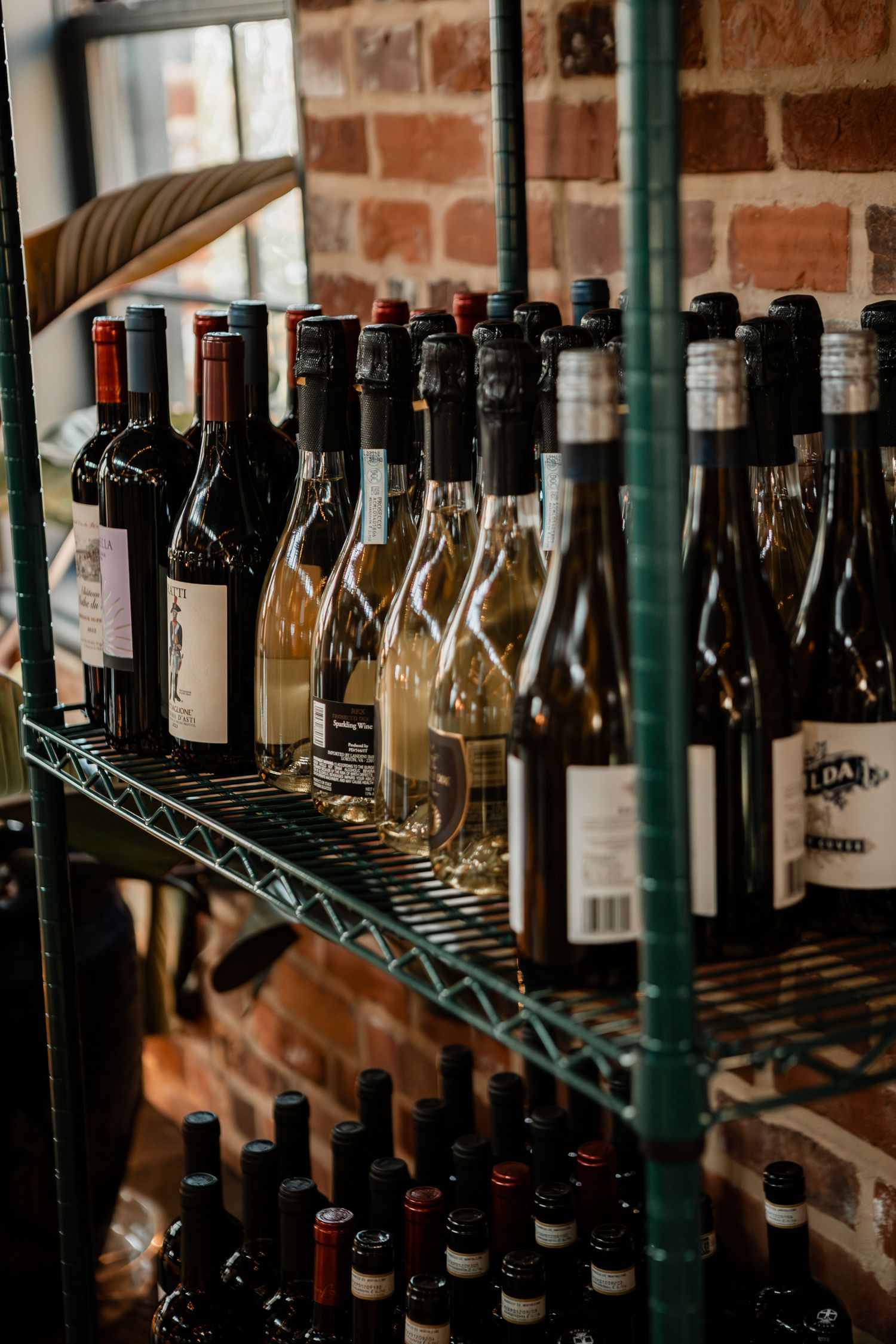 Wine bottles lined up on metal storage racks against rustic brick wall.