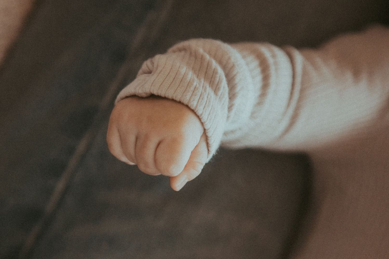 Close up of small baby hand reaching out against blurred background.