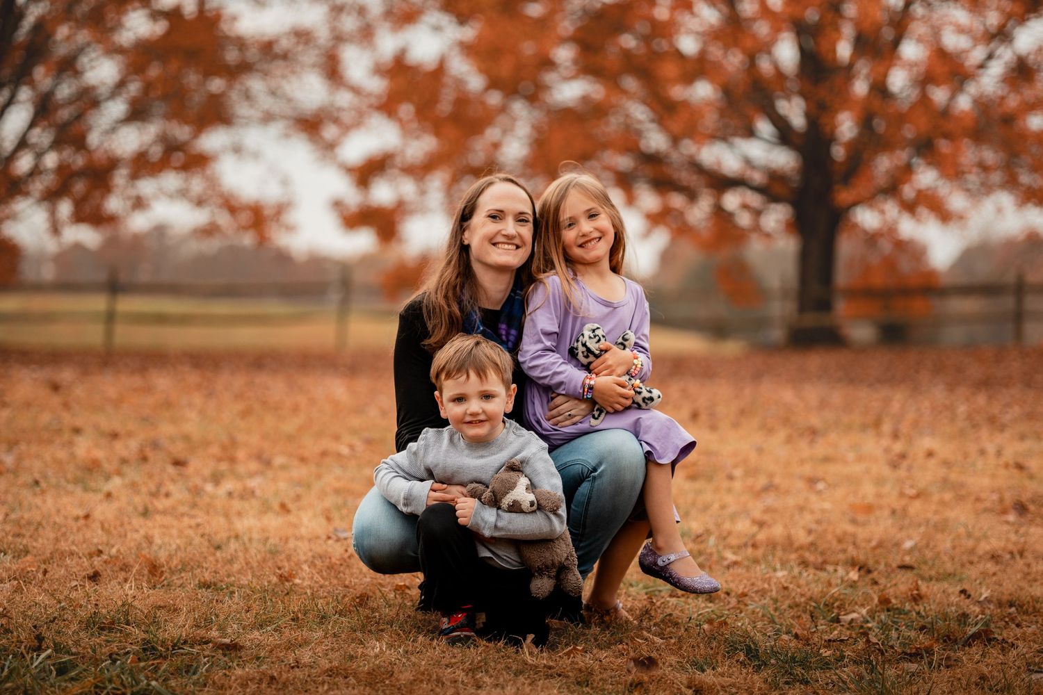 Autumn family photoshoot in a park with warm orange fall foliage in the background.