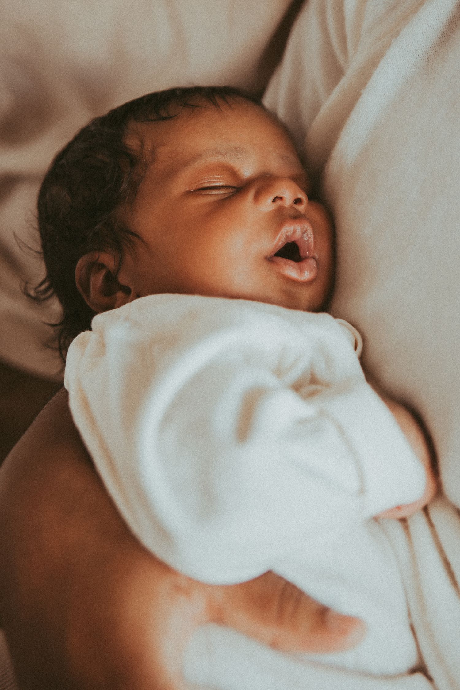 Peaceful sleeping baby wrapped in soft white blanket rests on cream-colored bedding.