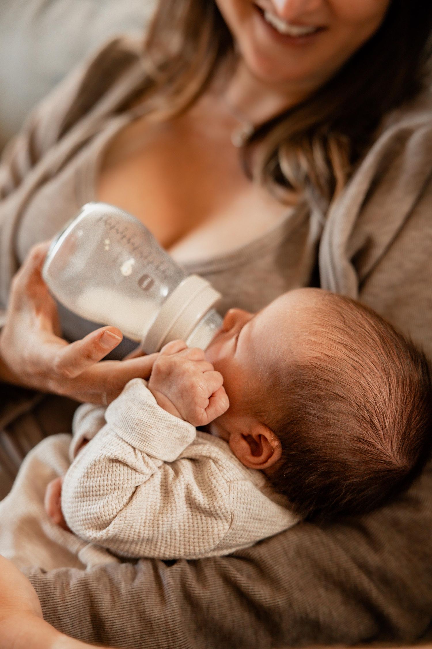 Mother bottle feeding her newborn baby while smiling warmly.