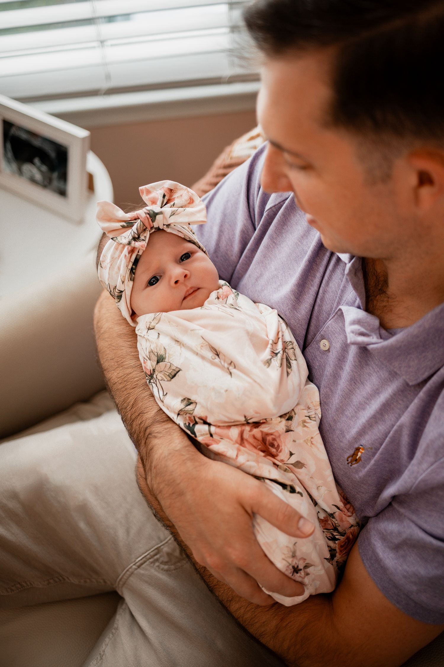 A tender moment as parents cradle their newborn baby wearing a floral headband in a series of intimate portraits.