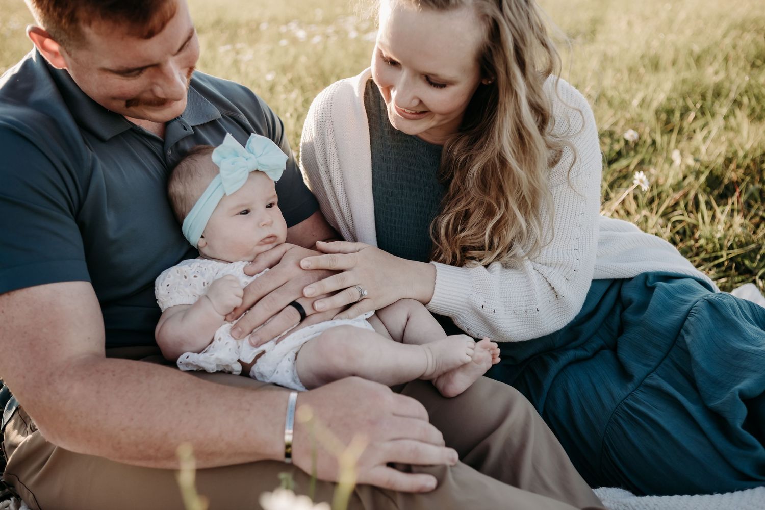 A family shares an intimate moment together while sitting in tall grass during golden hour.
