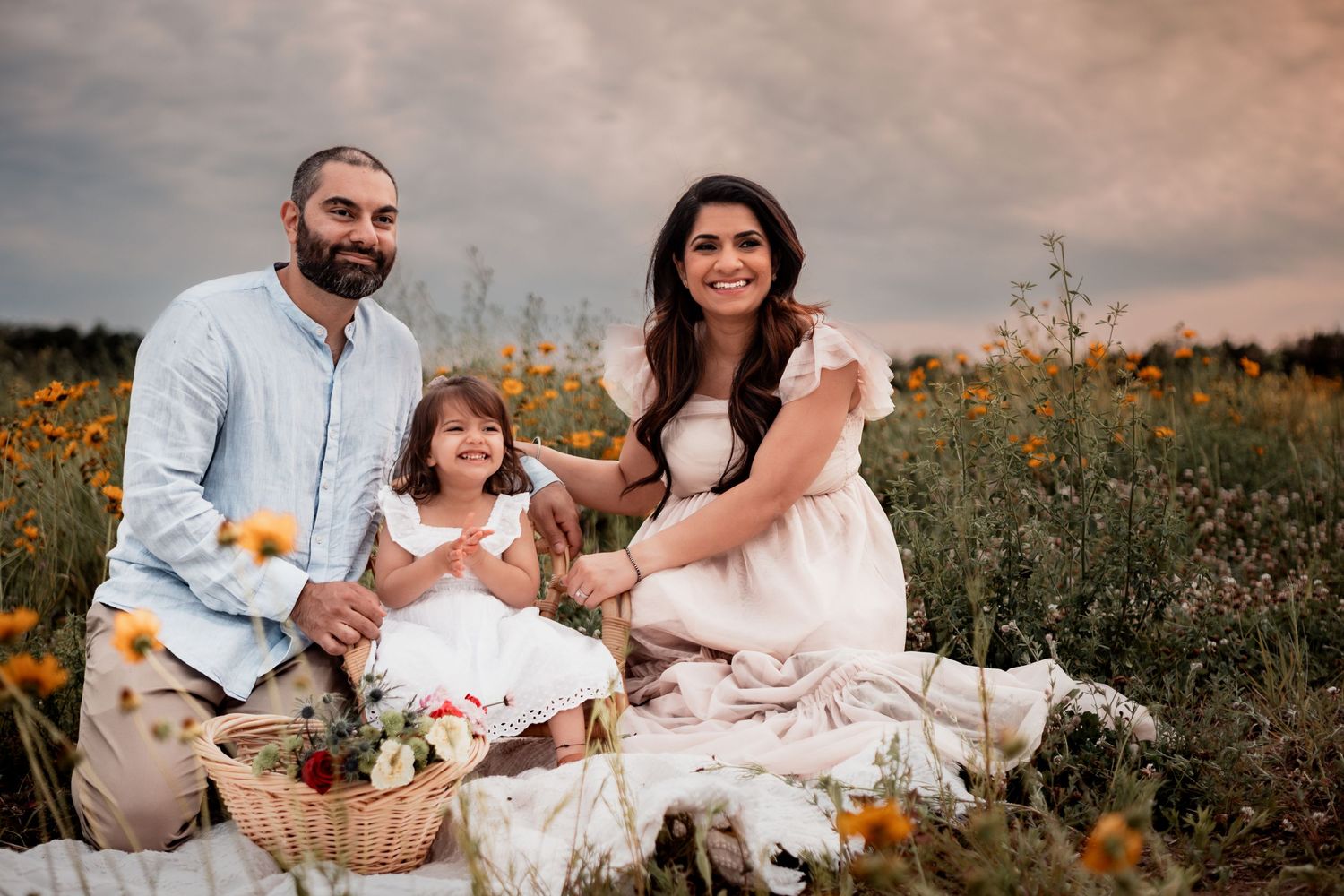 Family enjoys a picnic together on white blankets in a wildflower meadow during sunset.